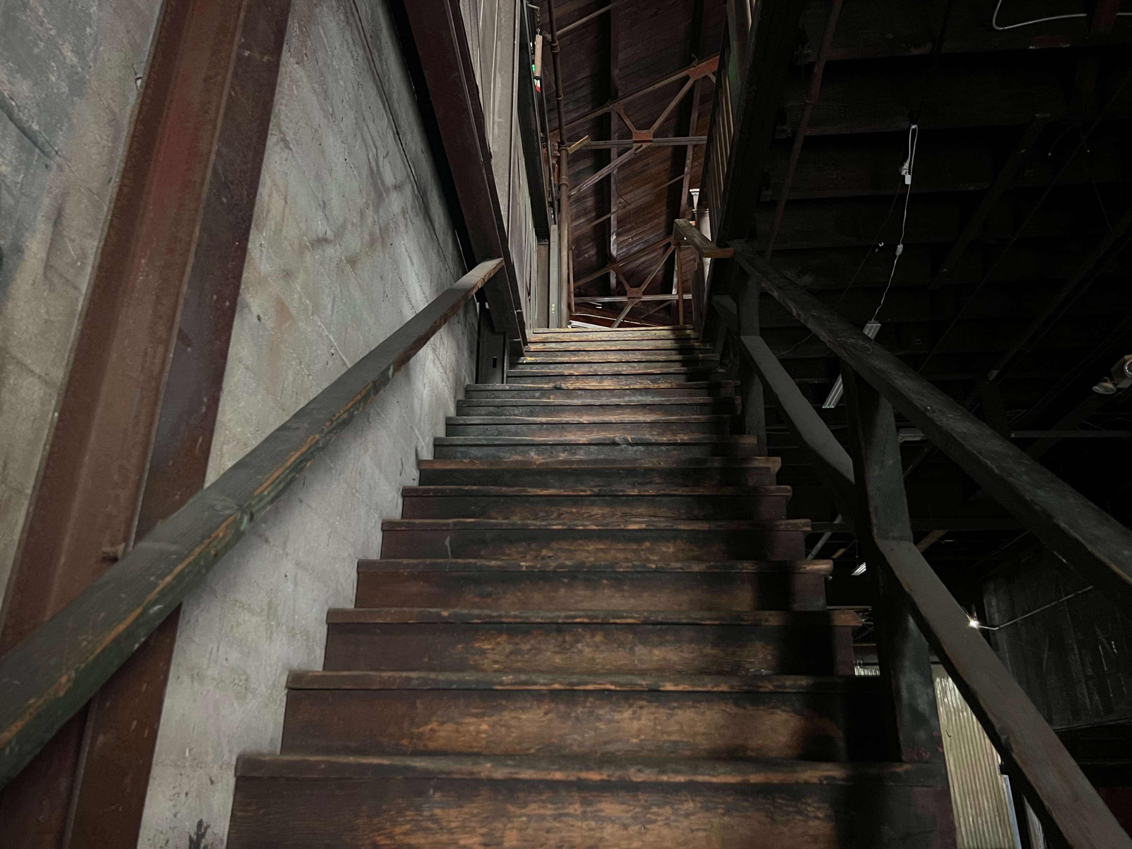 A wooden staircase leading upward in a dimly lit interior space.