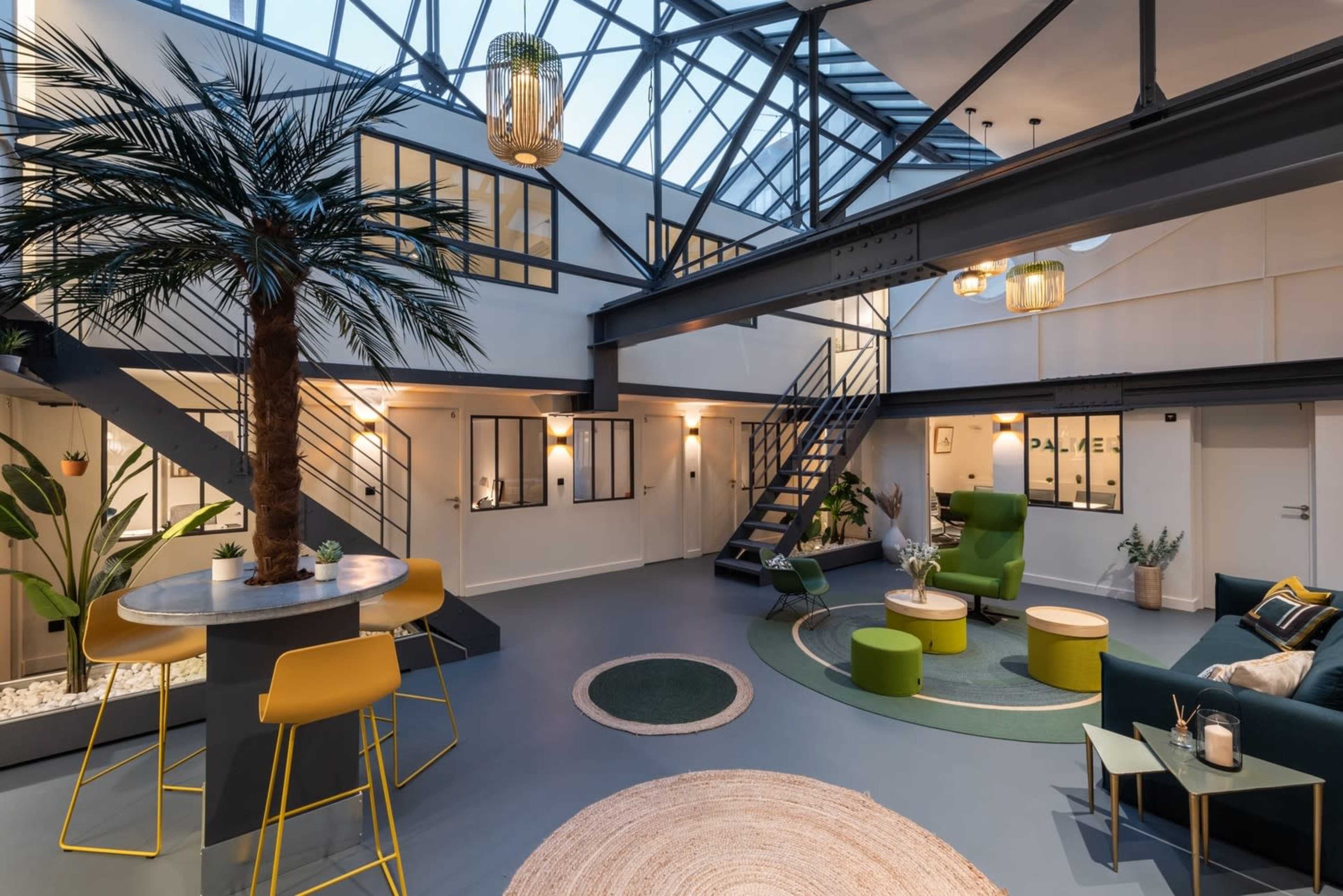 The image shows a modern, open-concept living space with a glass ceiling, featuring indoor plants, a staircase, seating areas, and circular rugs.