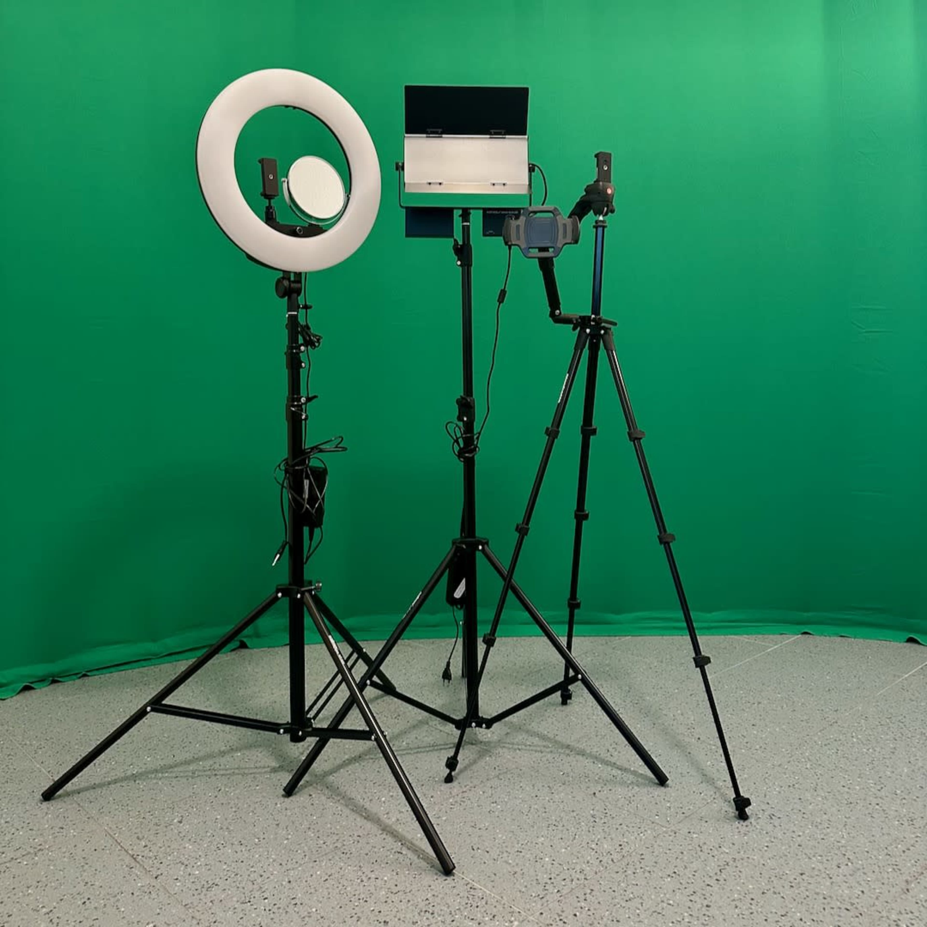 The image shows a green backdrop with a ring light and a camera setup on tripods positioned in front of it.