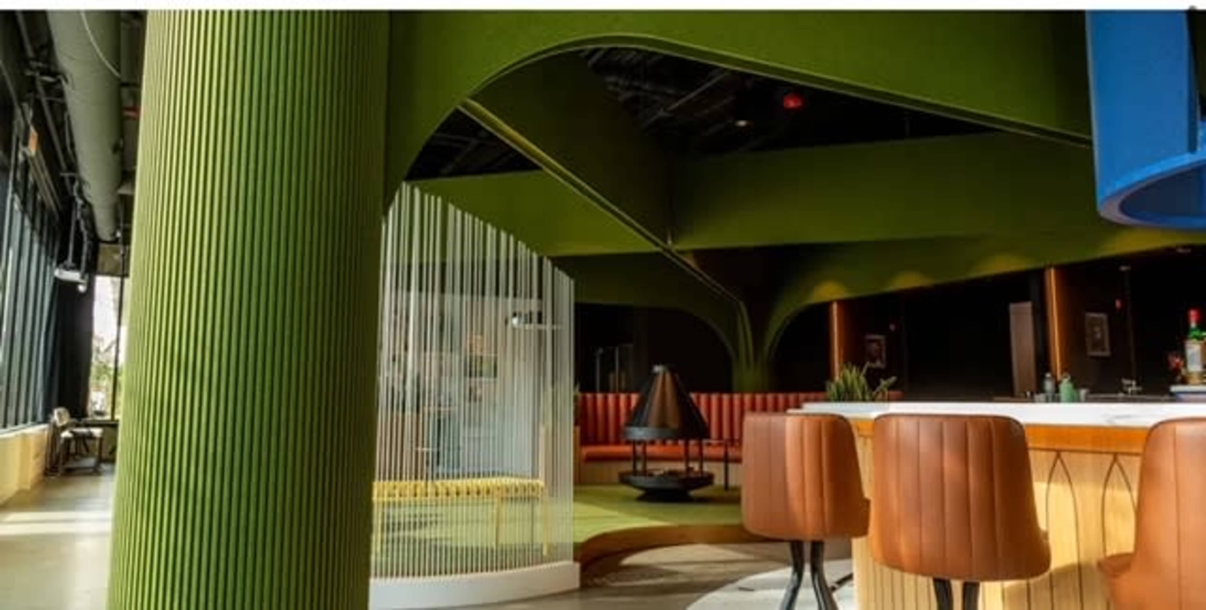A modern, stylish bar area with green architectural elements and brown seating.