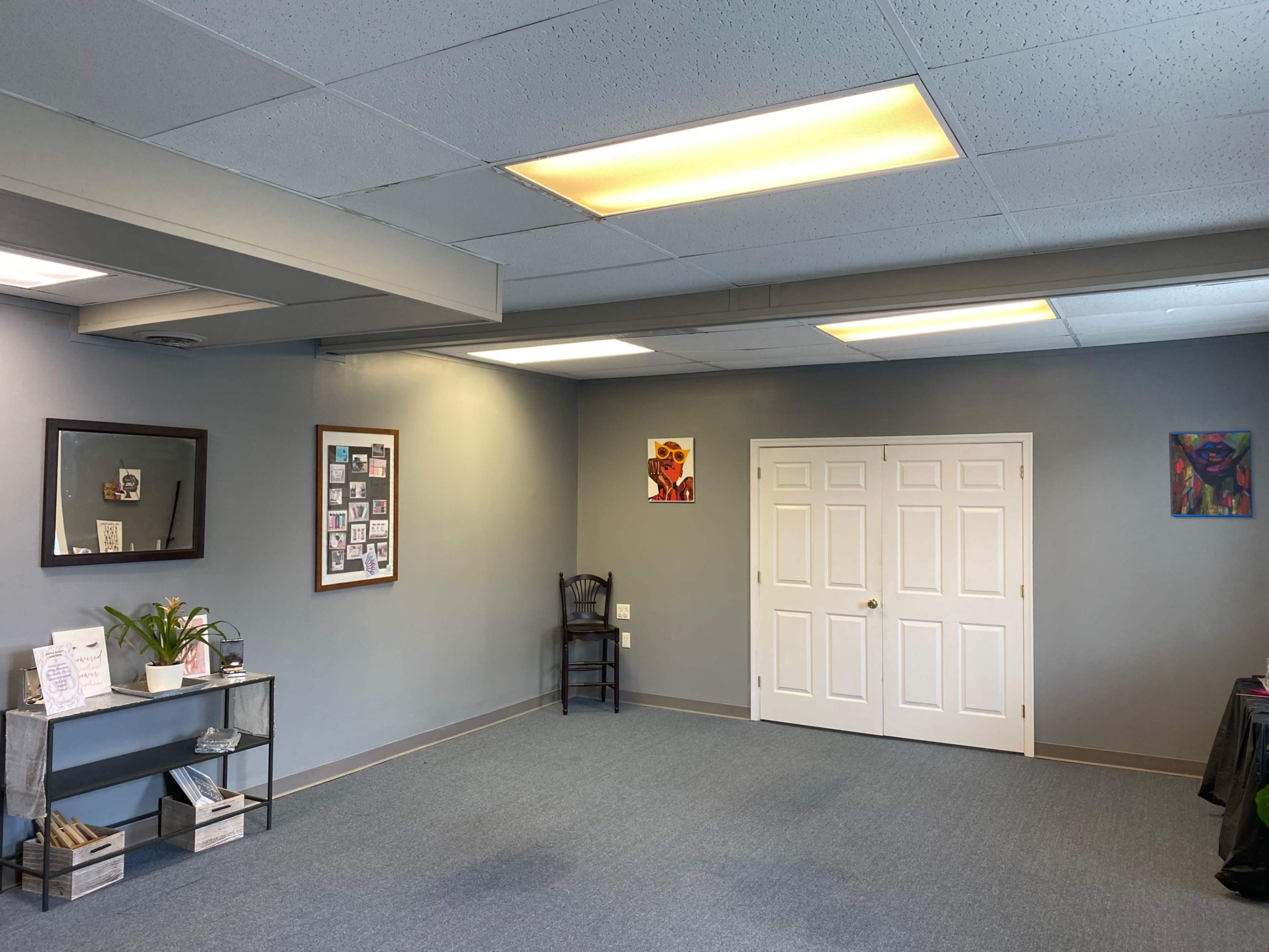 The room features gray walls, a blue carpet, a chair in the corner, and two paintings on the walls.