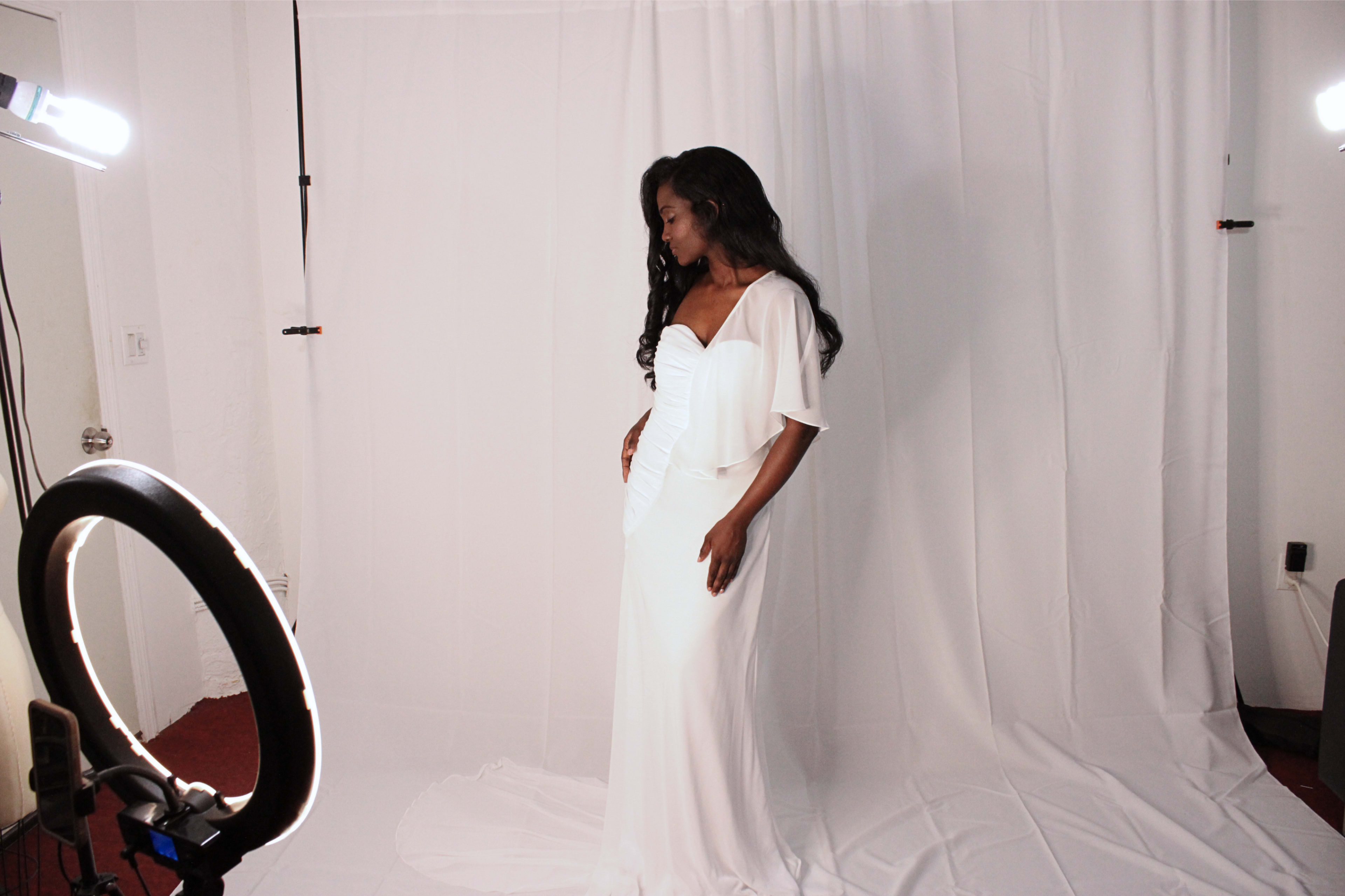A woman in a white dress poses in front of a white backdrop with studio lighting.