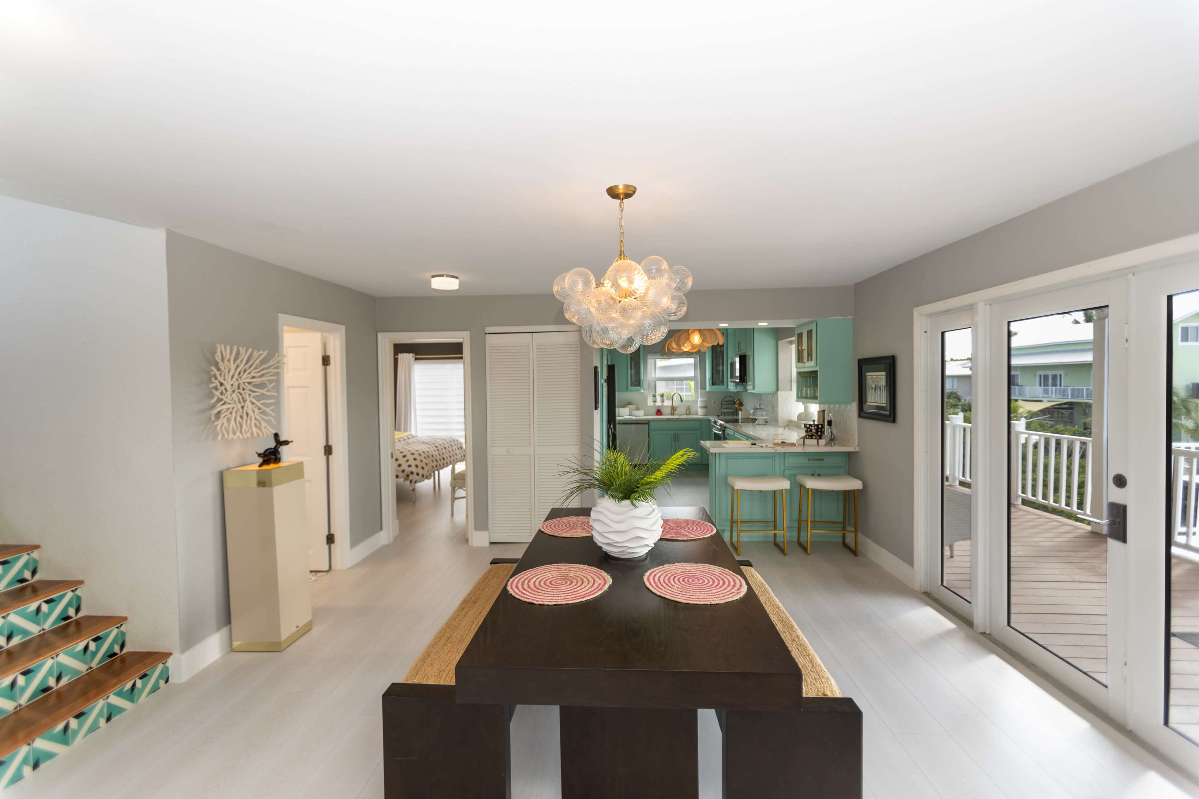 The image shows a modern dining area with a dark wooden table, a round light fixture, and a green kitchen visible in the background.