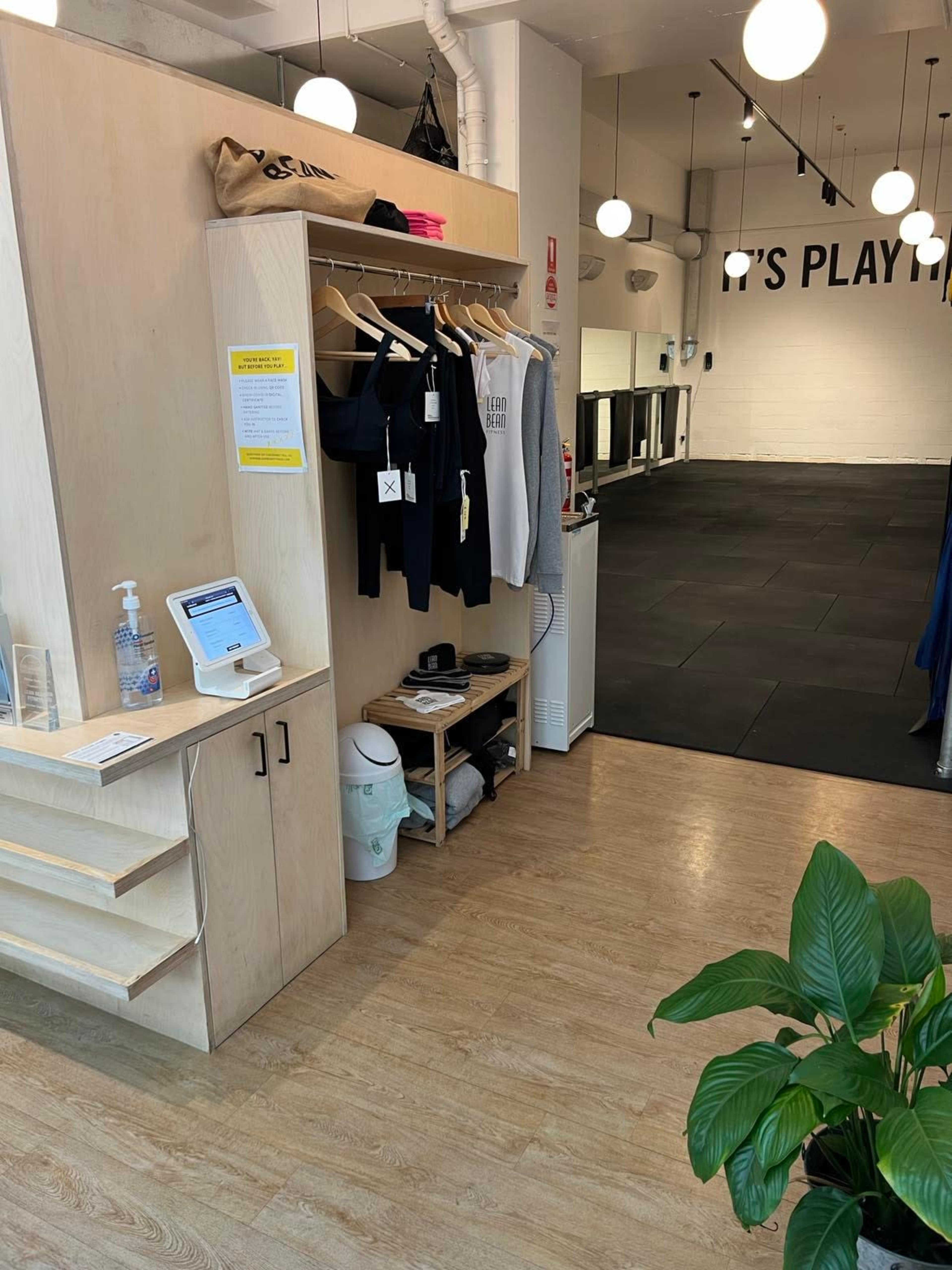 The interior of a fitness studio with a neatly arranged reception area featuring clothing racks and a hand sanitizer station.