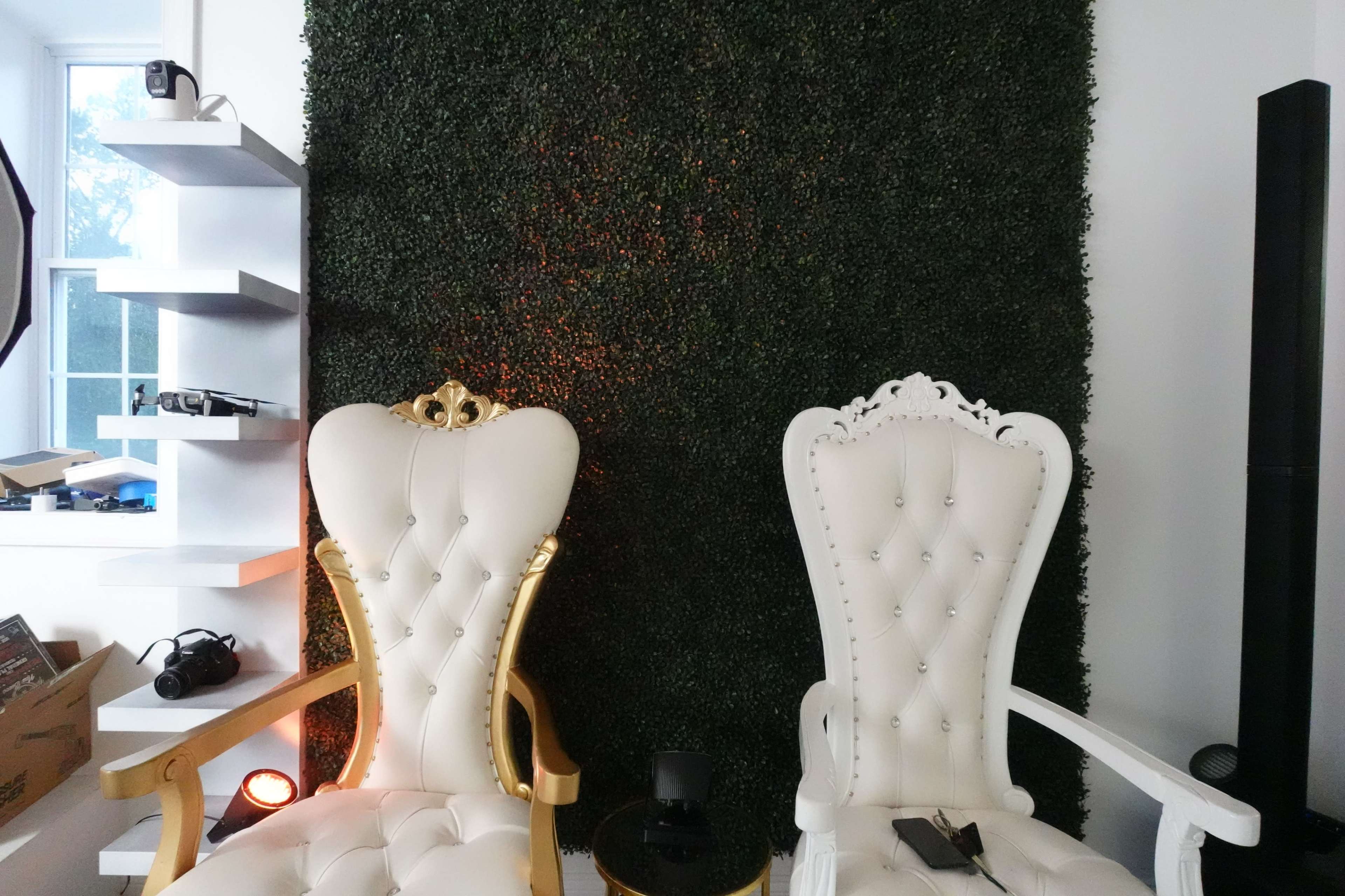 Two ornate white chairs with gold accents positioned against a green, textured wall.