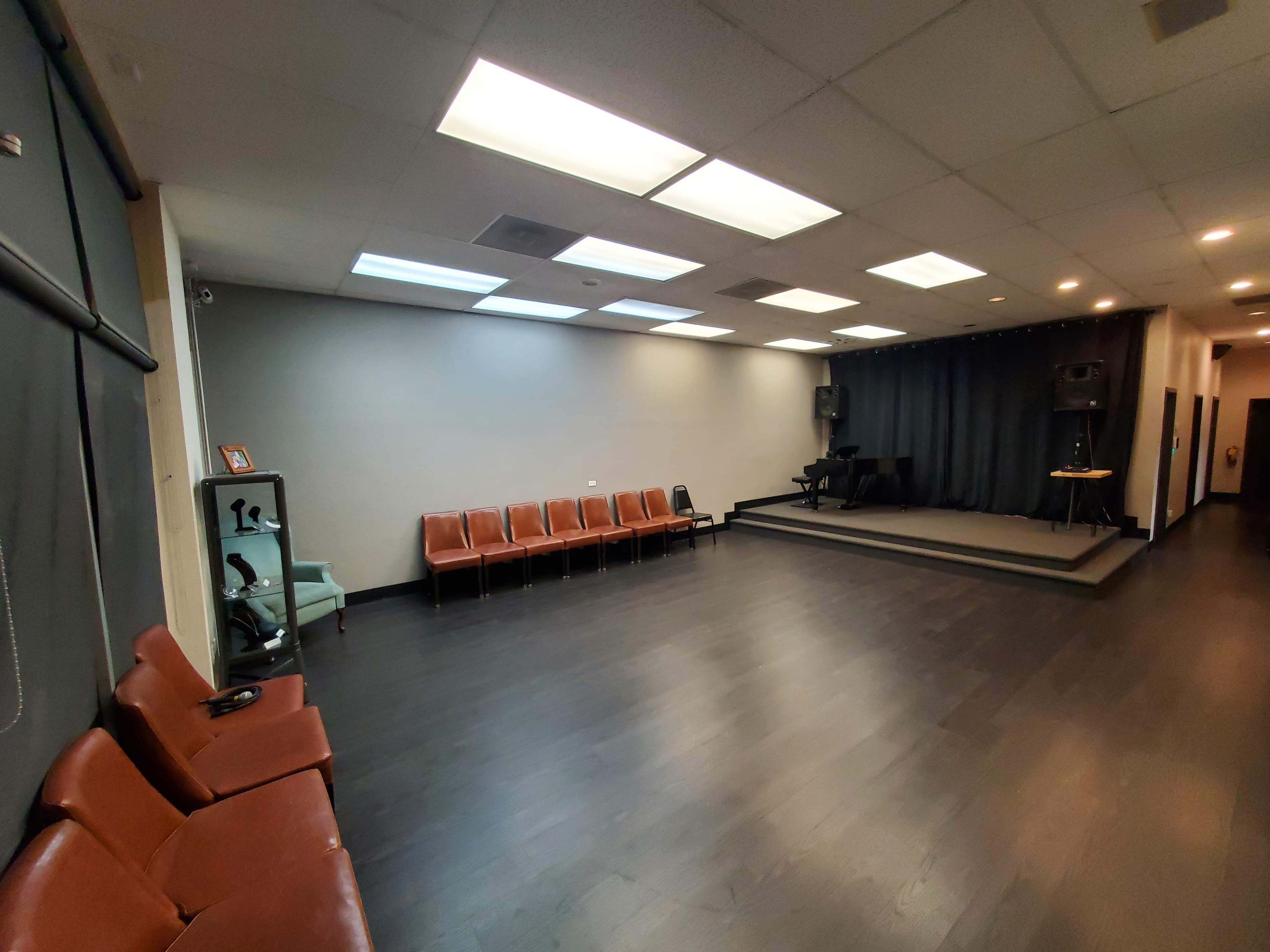 The image shows a spacious room with a stage, seating along one wall, and a polished floor.