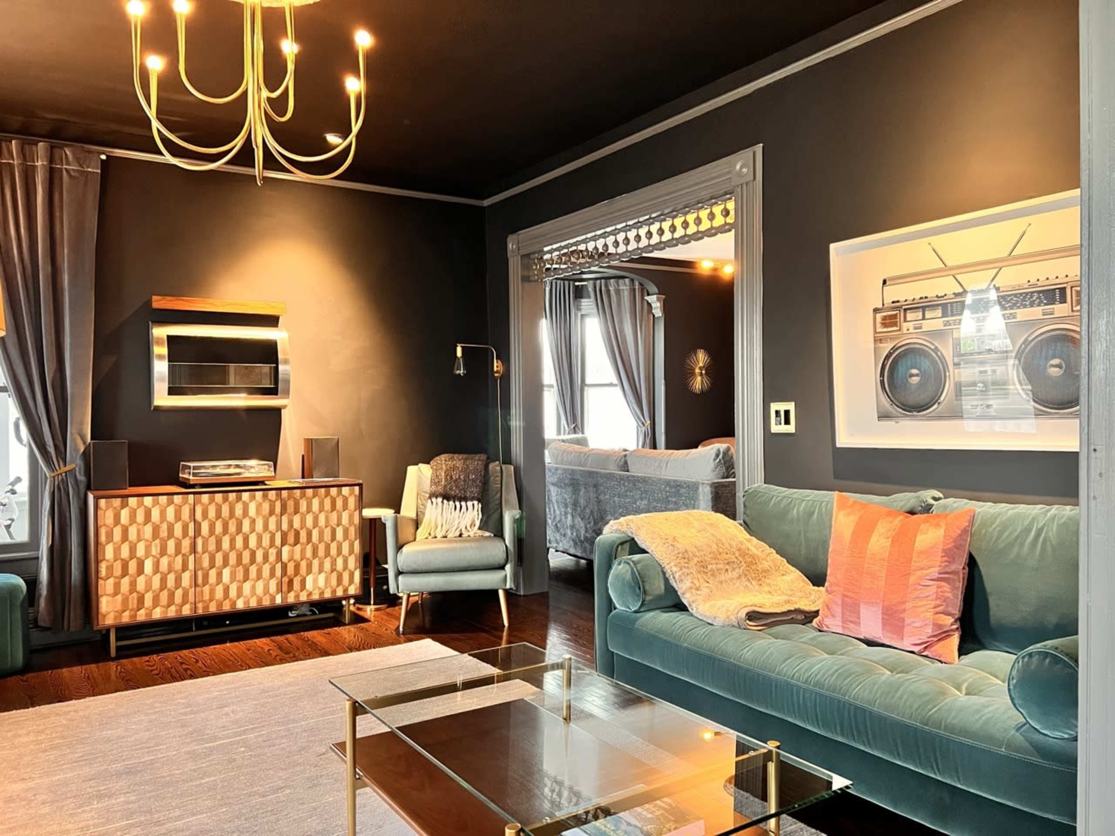 A modern living room featuring a teal sofa, a glass coffee table, and a wall decorated with an art piece of a vintage boombox.