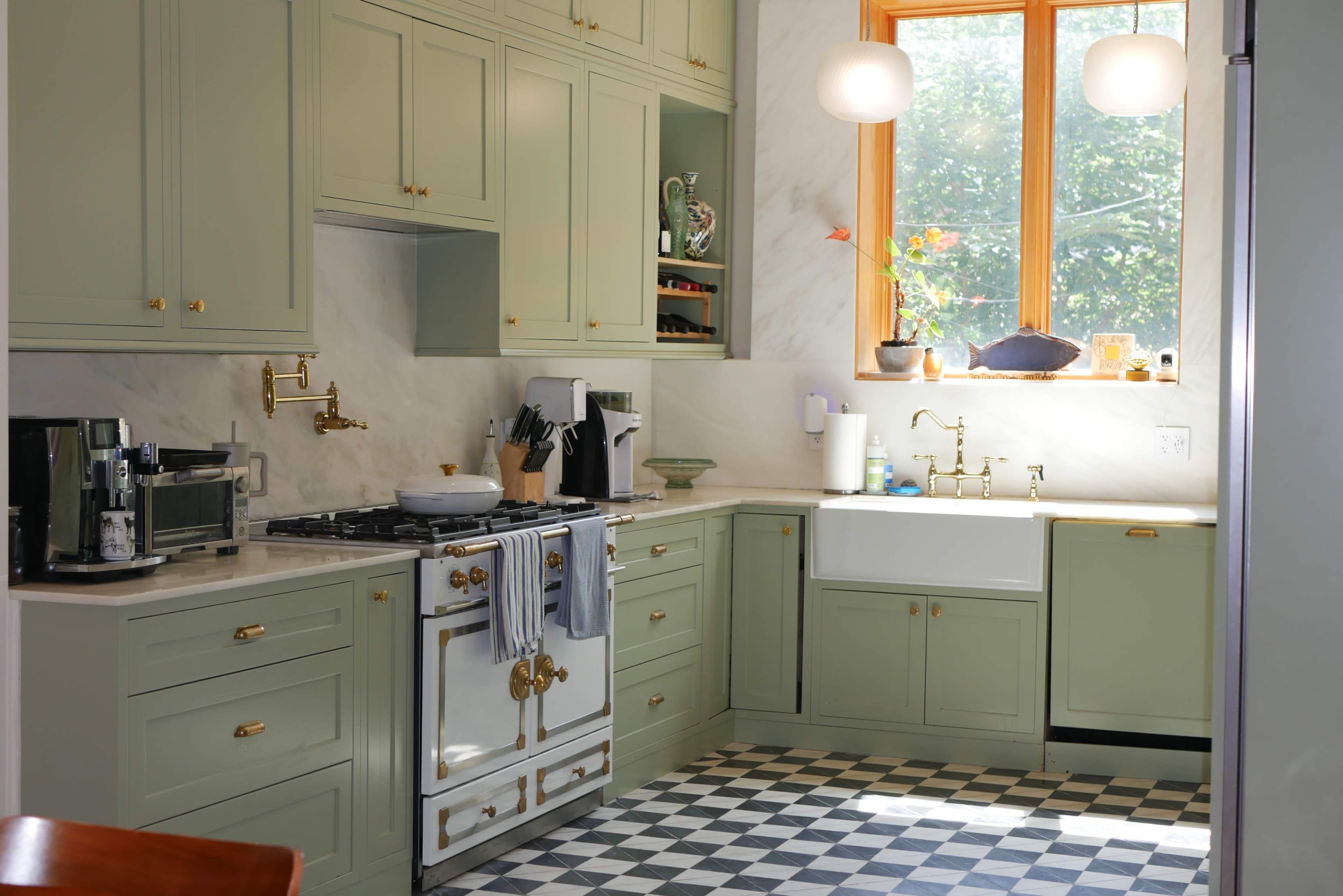 The kitchen features green cabinets, a large farmhouse sink, a checkered floor, and a window that provides natural light.