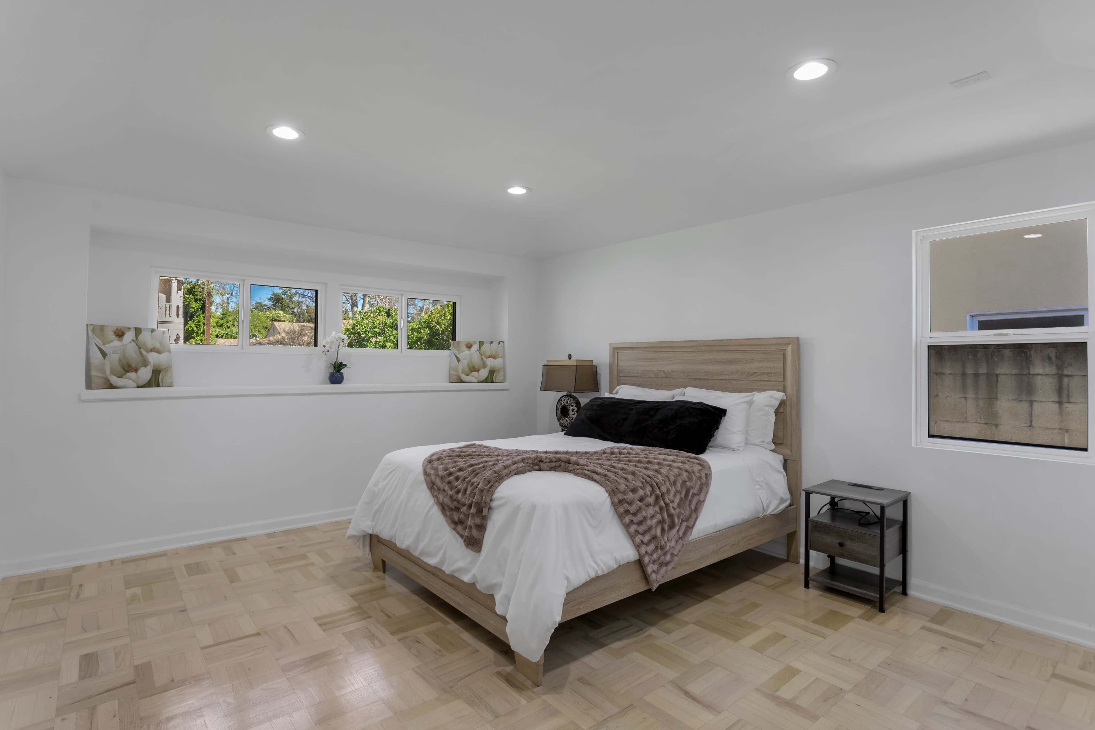 A minimalistic bedroom with a bed, nightstand, and large windows allowing natural light.