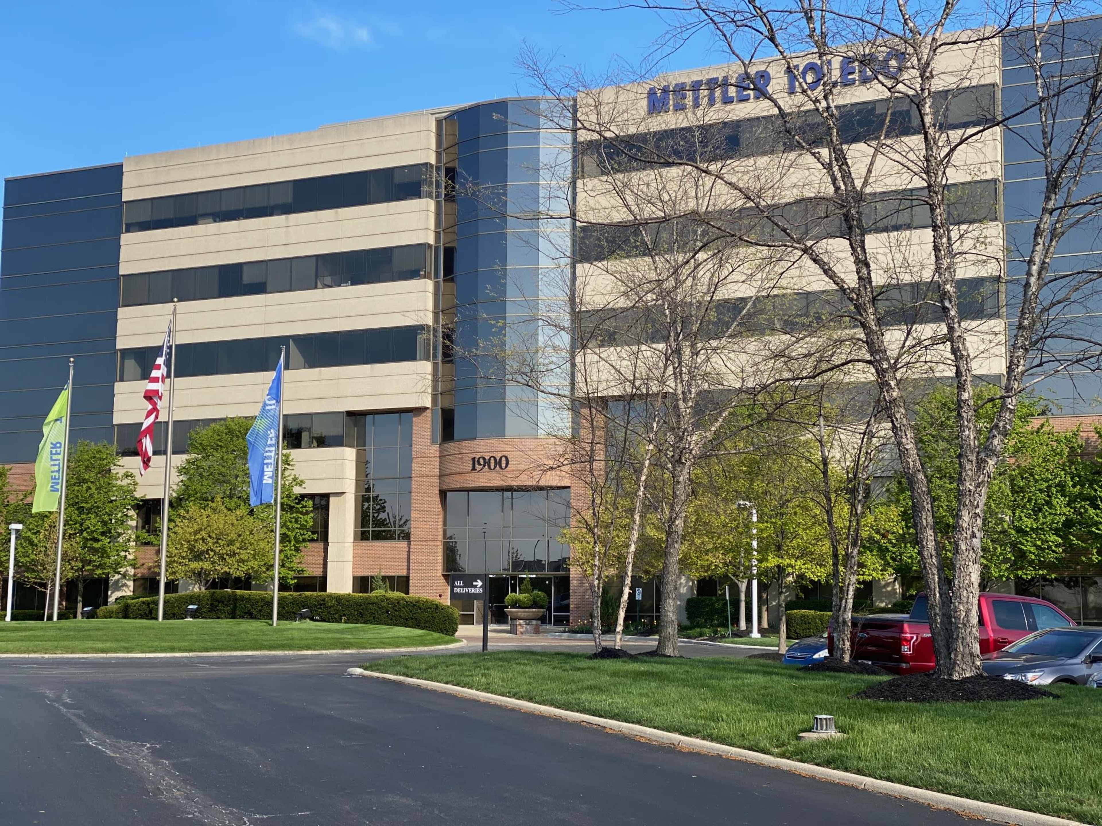 The exterior of the Mettler Toledo building, a multi-story glass office complex with a landscaped entrance and several flags displayed.