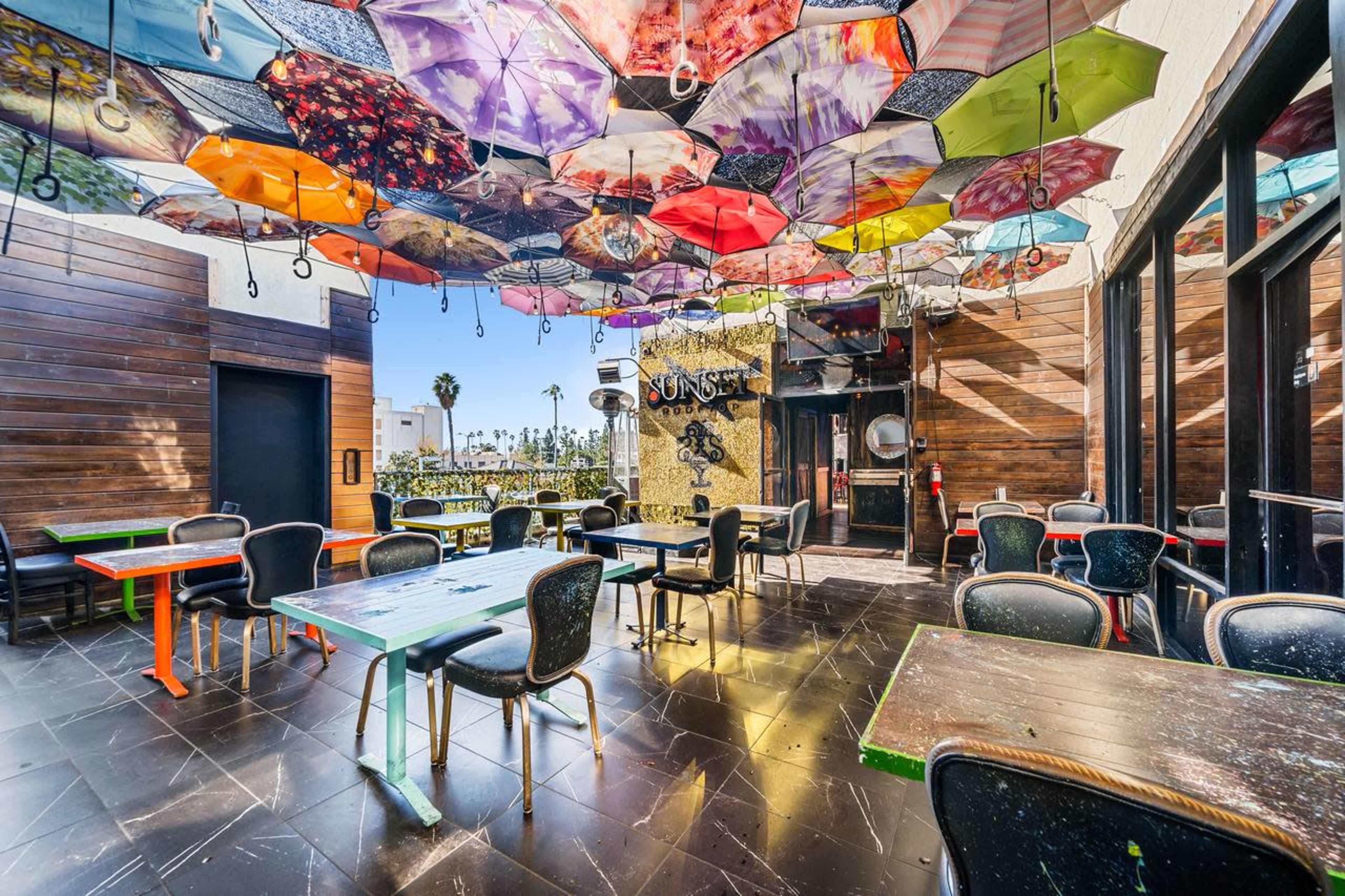 The image shows a restaurant or cafe with tables and chairs arranged below a ceiling decorated with colorful umbrellas.