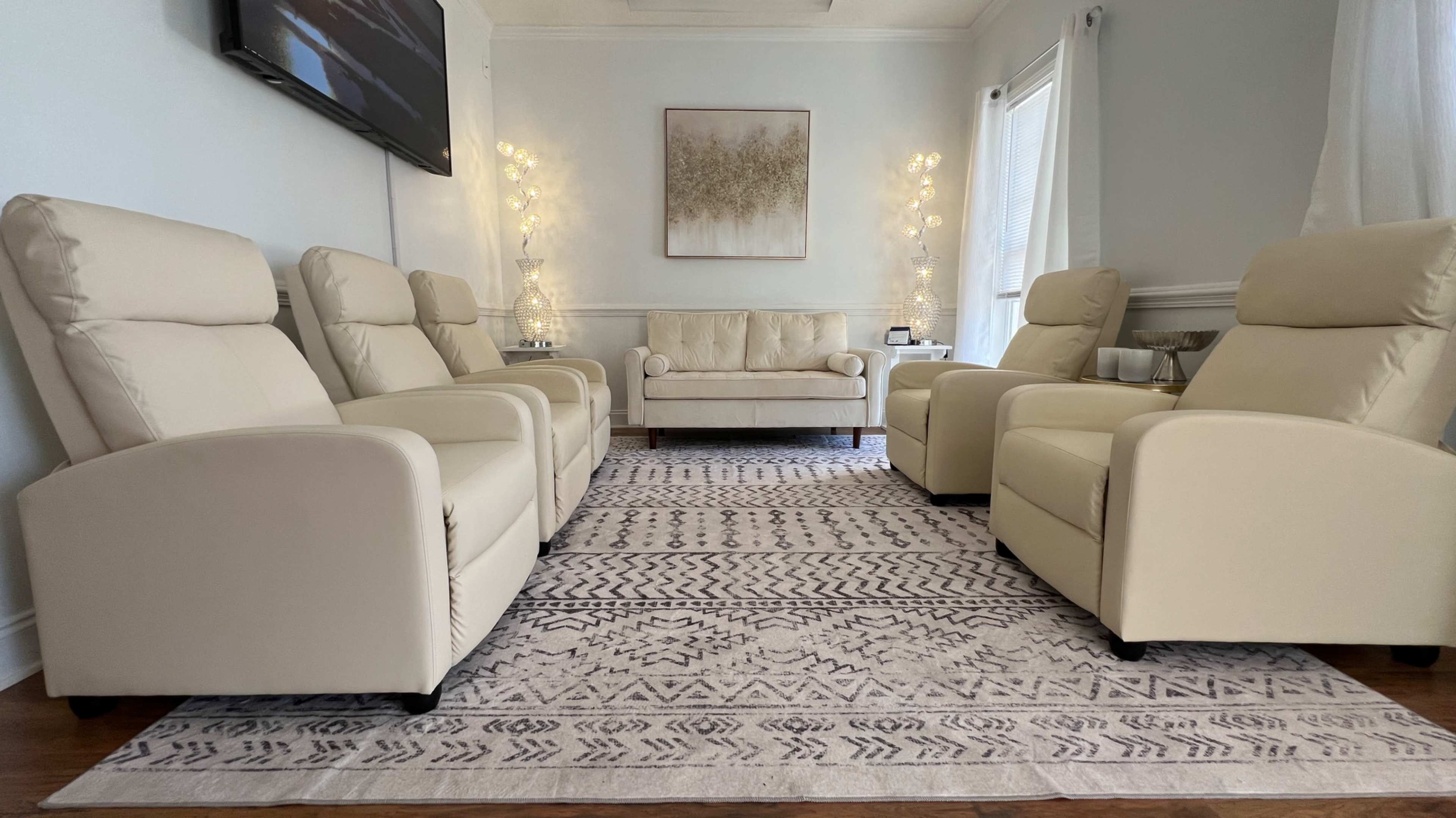 The image shows a neatly arranged living room with cream-colored recliner chairs, a sofa, and a decorative rug.