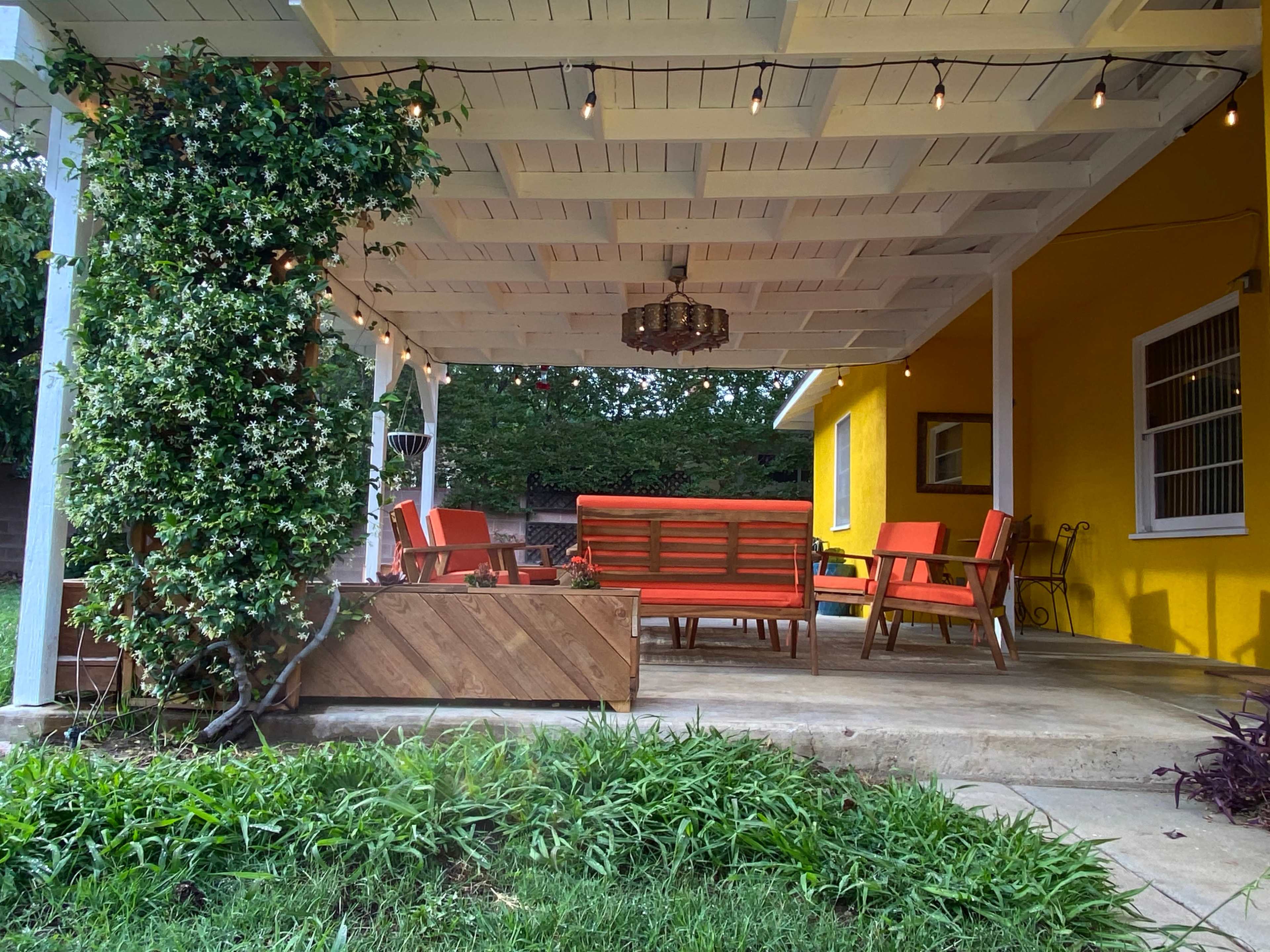 A covered patio with orange furniture, string lights overhead, and a yellow wall in the background.