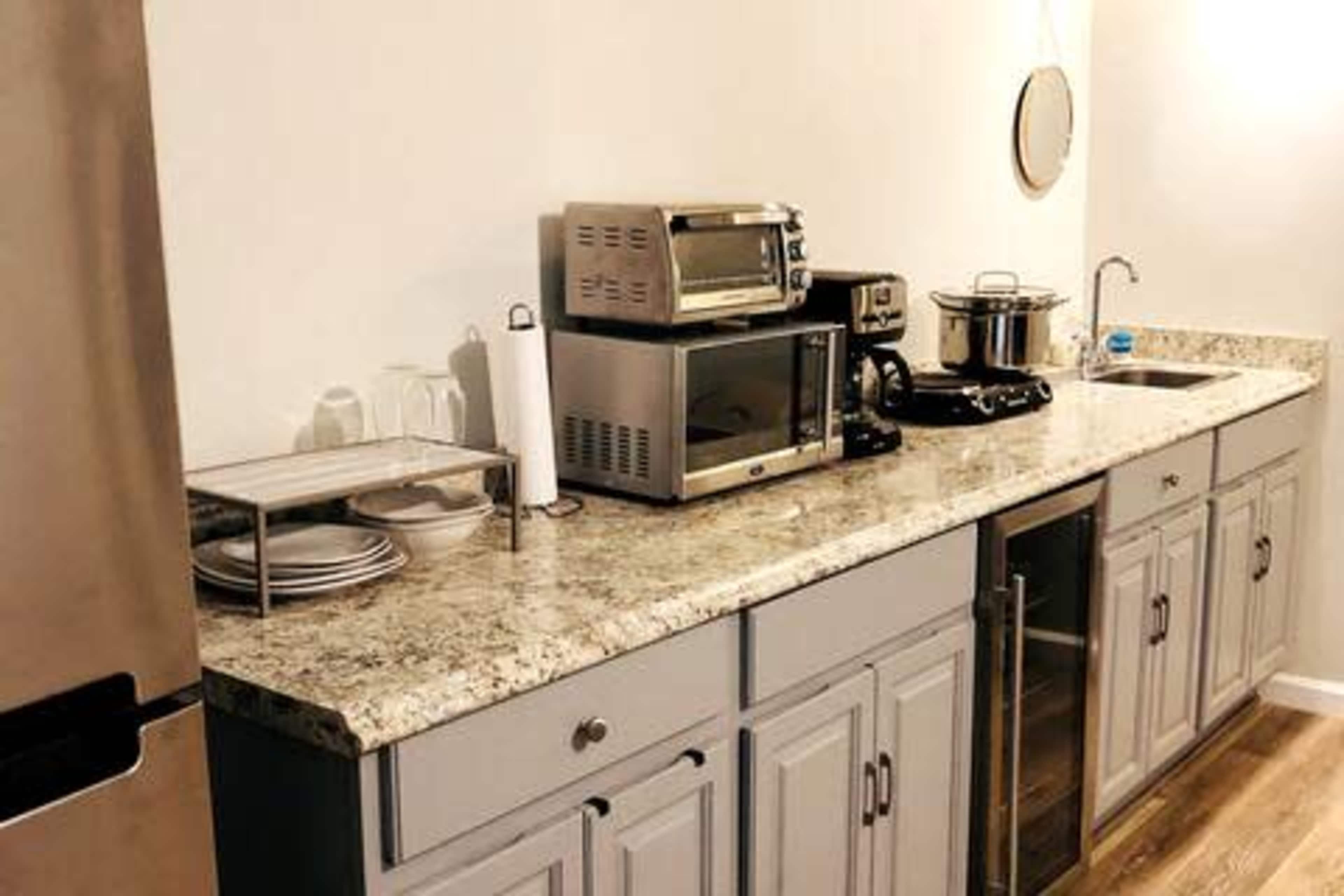 A kitchen countertop with a microwave, toaster oven, coffee maker, and sink, along with plates and glassware on a metal rack.