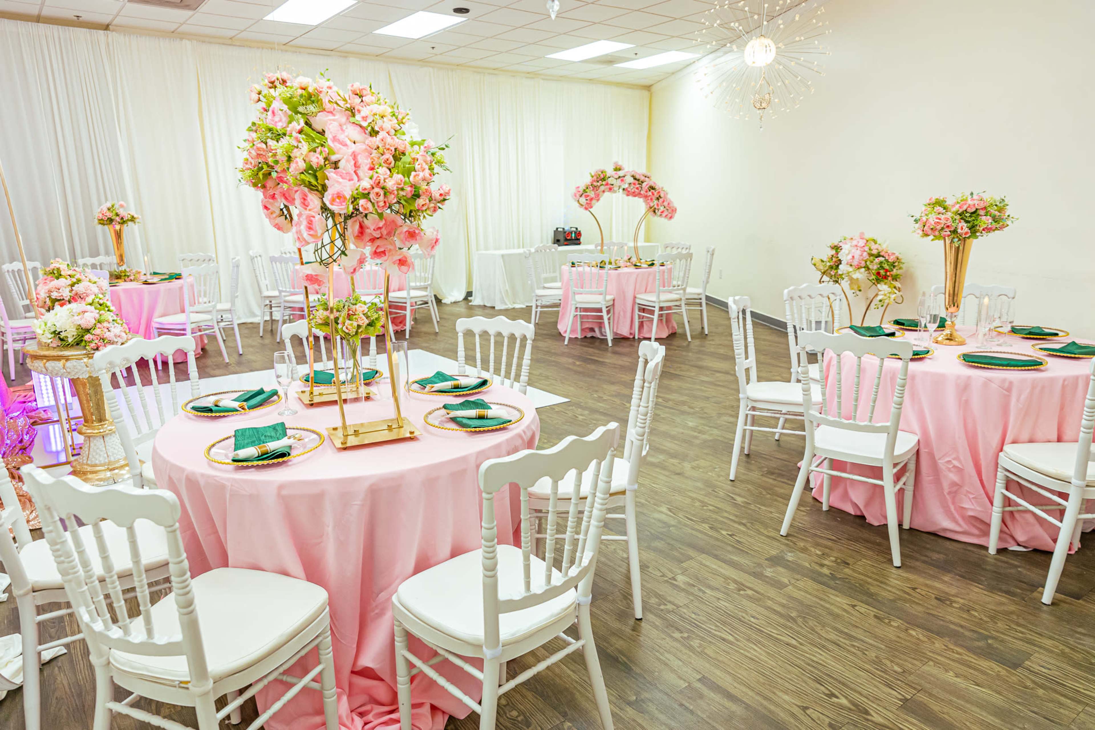 A banquet hall set up for an event, featuring round pink tablecloths, white chairs, and floral centerpieces.
