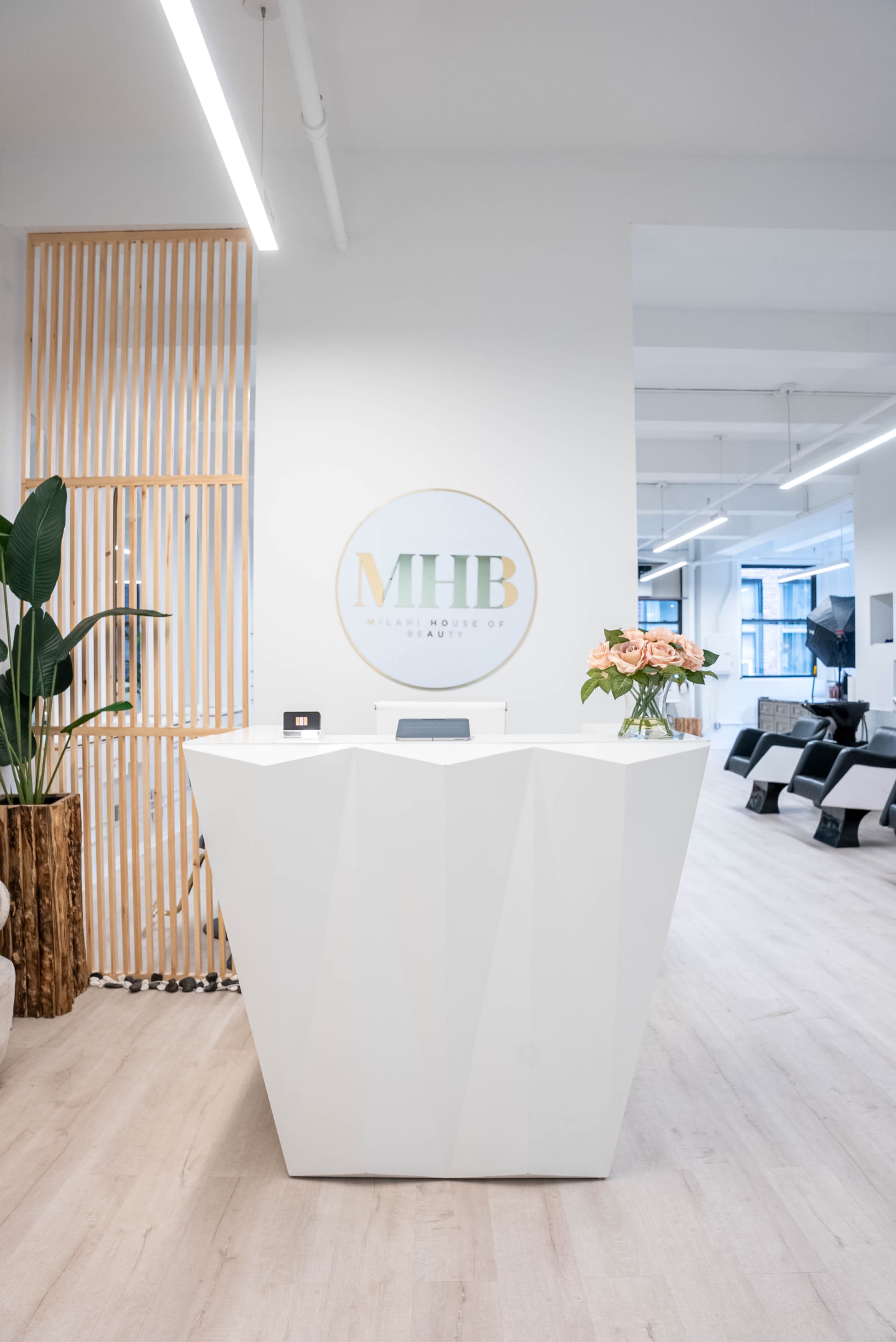 A modern reception area featuring a white geometric desk with a flower vase, wooden accents, and a circular logo on the wall.