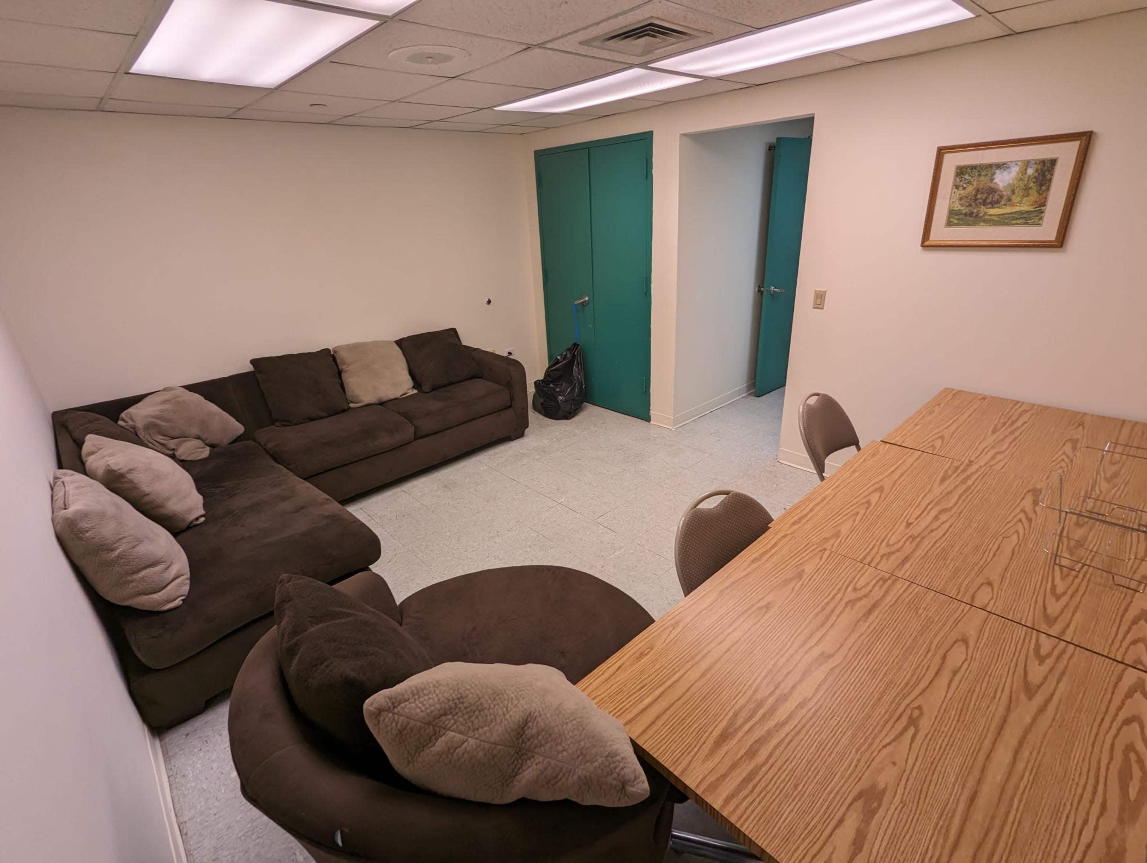 The image shows a small, empty room with a couch, a round chair, and a wooden table surrounded by chairs.