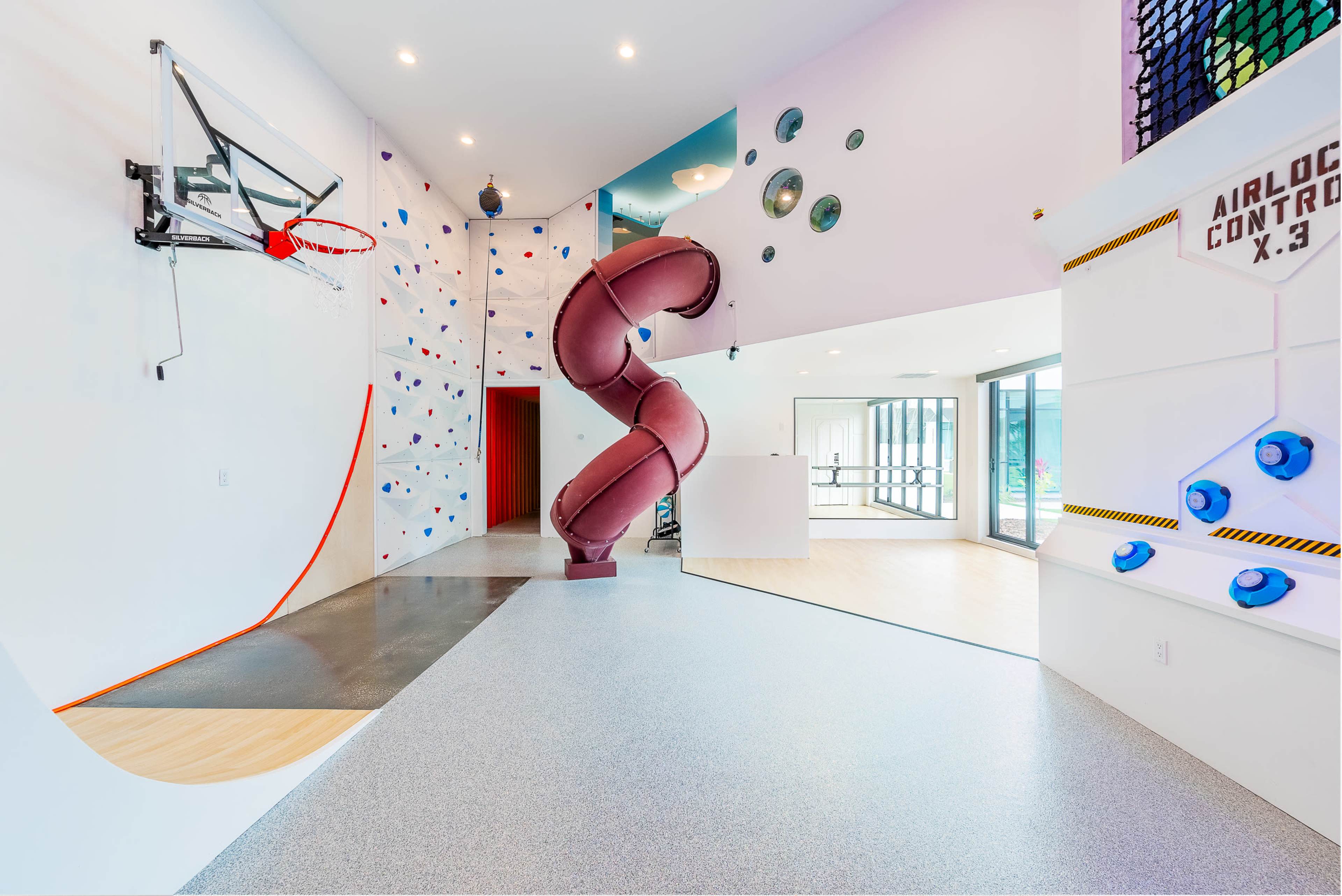 The image showcases a modern recreational space featuring a climbing wall, a basketball hoop, and a spiral slide.