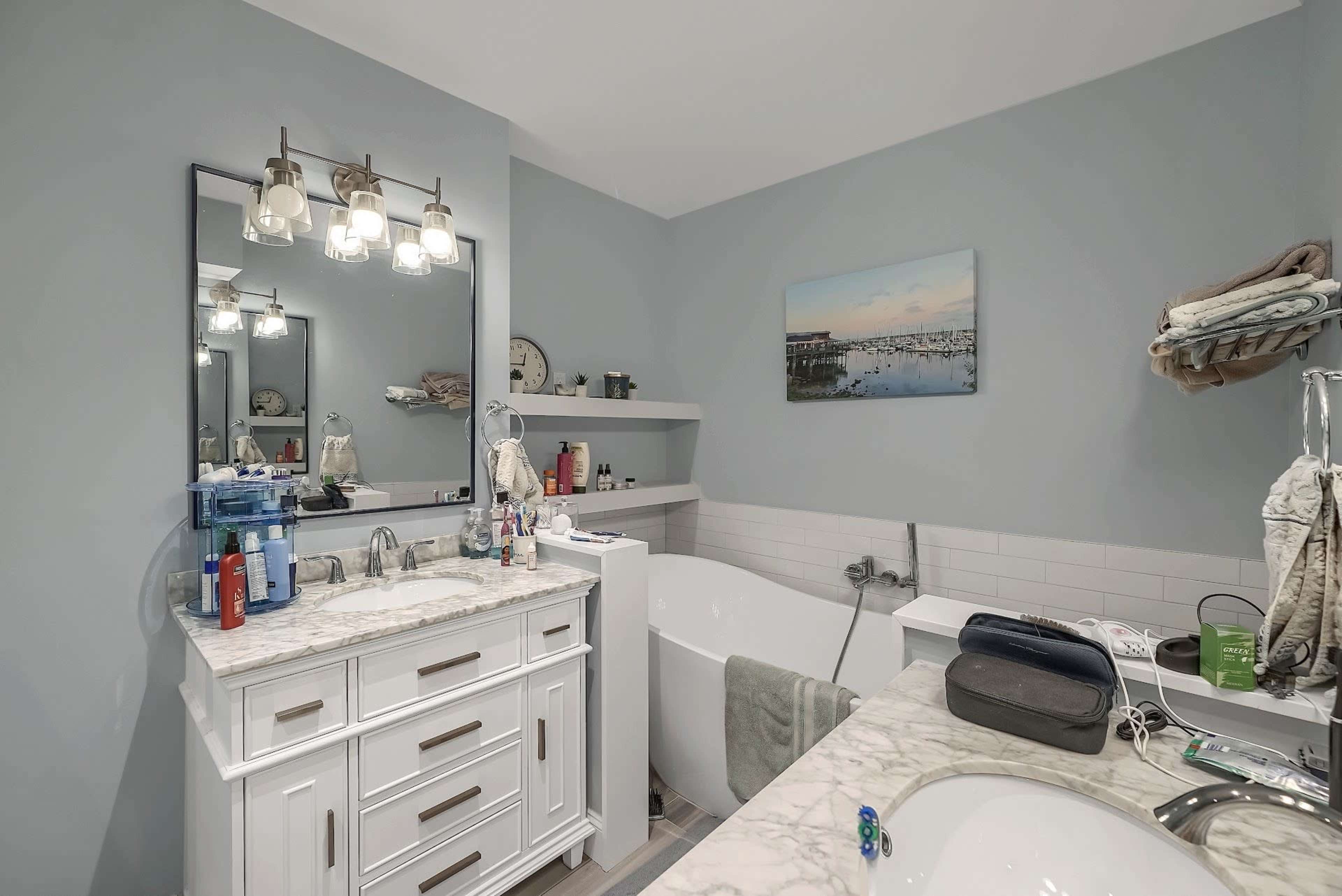 A modern bathroom featuring a white double vanity with a marble countertop, a freestanding bathtub, and light gray walls.