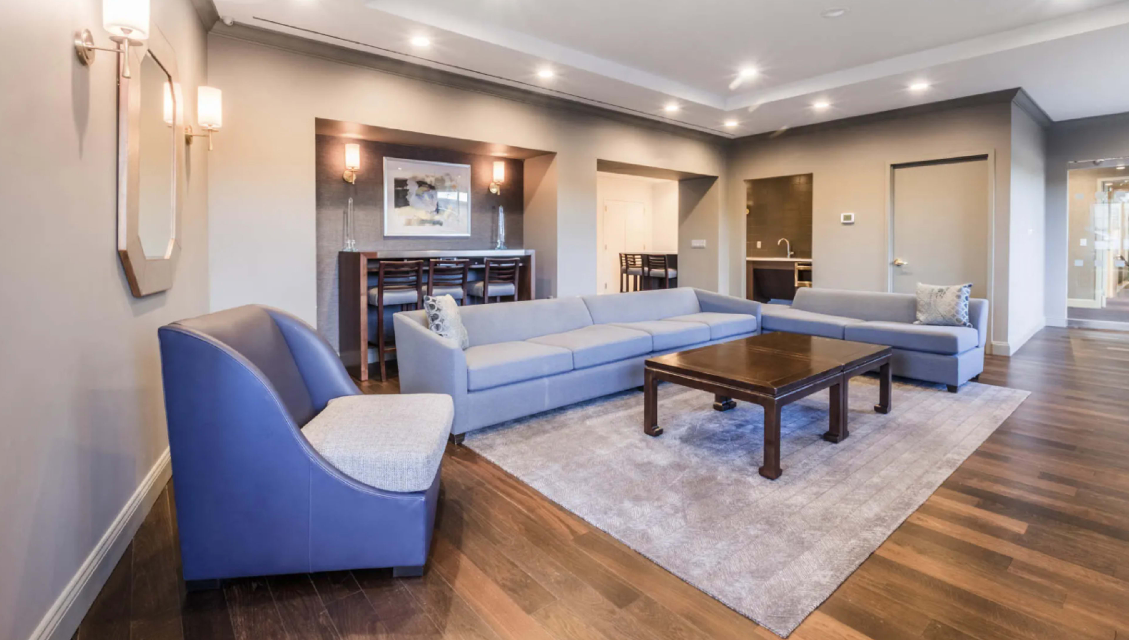 A modern living room with a sectional sofa, a wooden coffee table, and a bar area in the background.