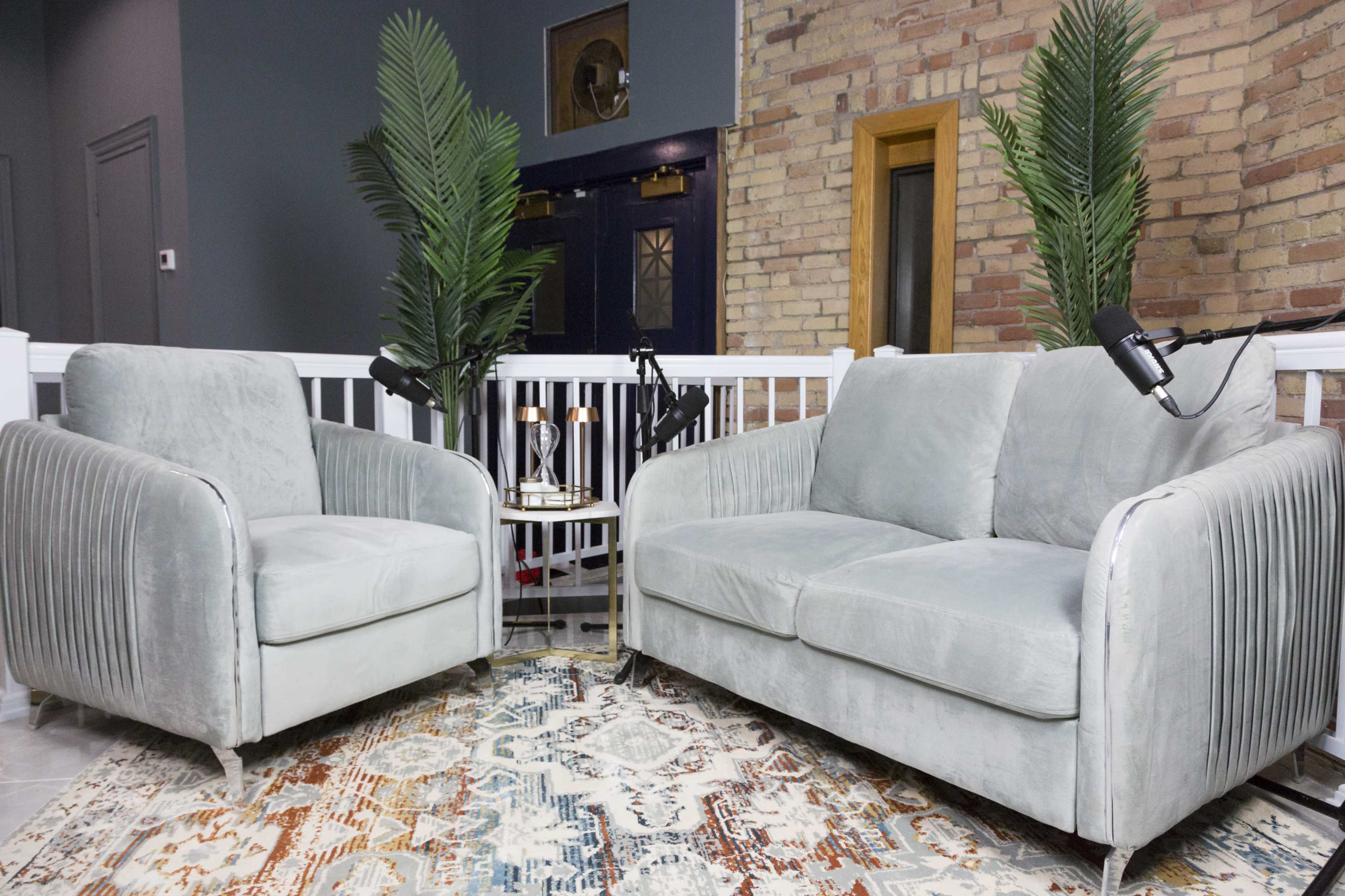A light-colored sofa and armchair with ribbed design, placed near a small table with two lamps and surrounded by decorative plants in an indoor setting.