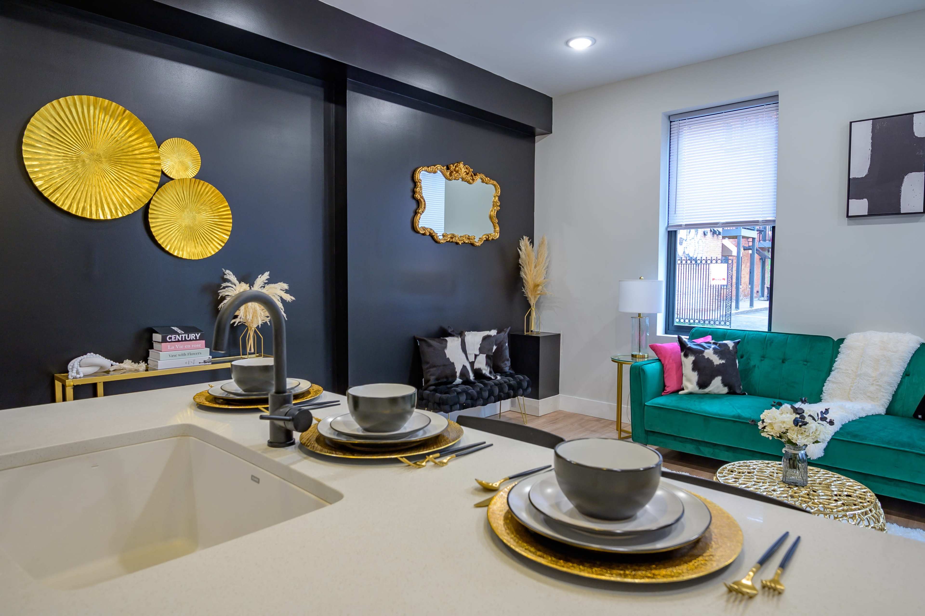 A stylish living area featuring a green sofa, decorative gold wall art, and a dining setup with plates and bowls on a countertop.