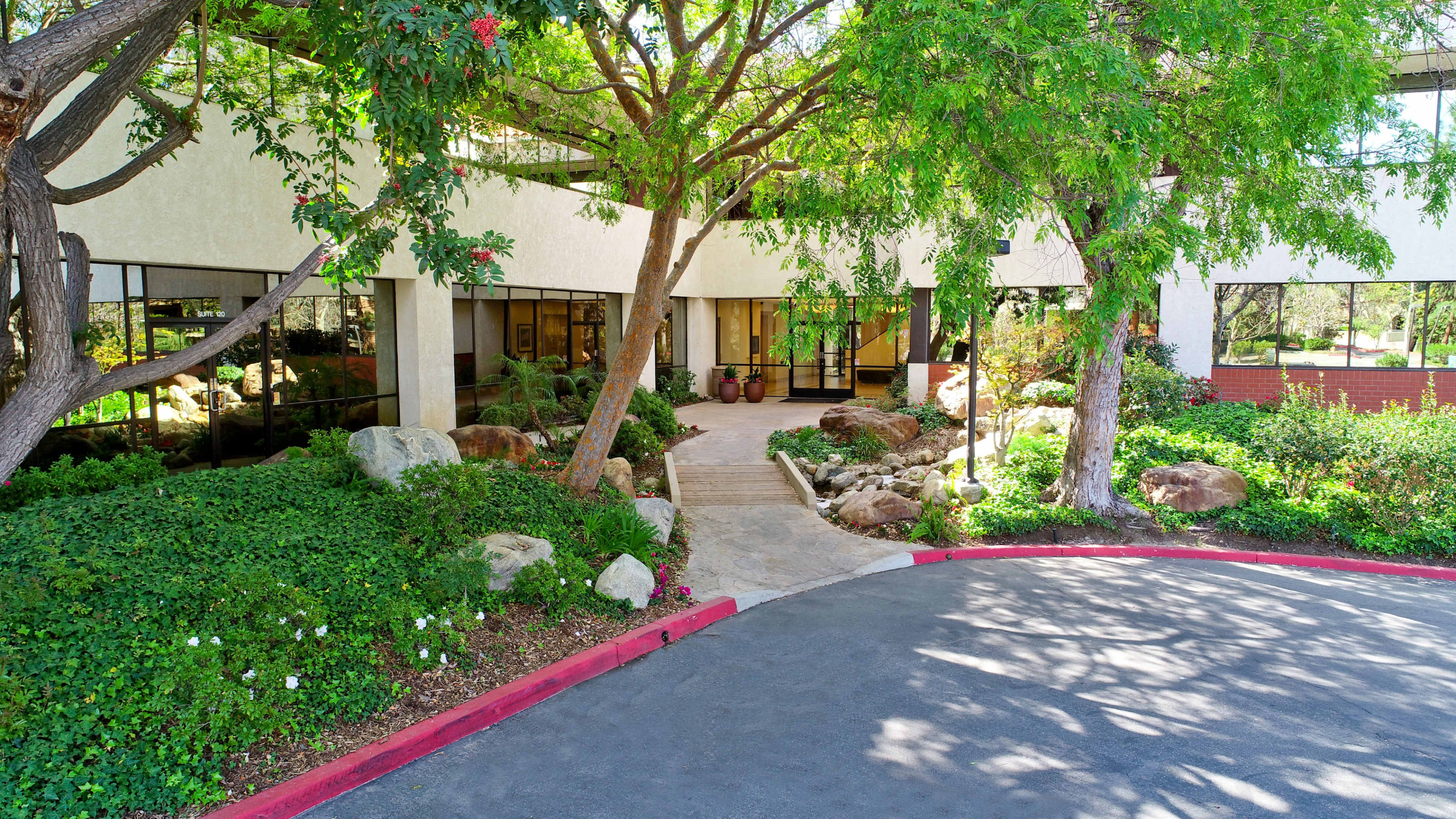 An entrance to a building surrounded by landscaped greenery, rocks, and trees.