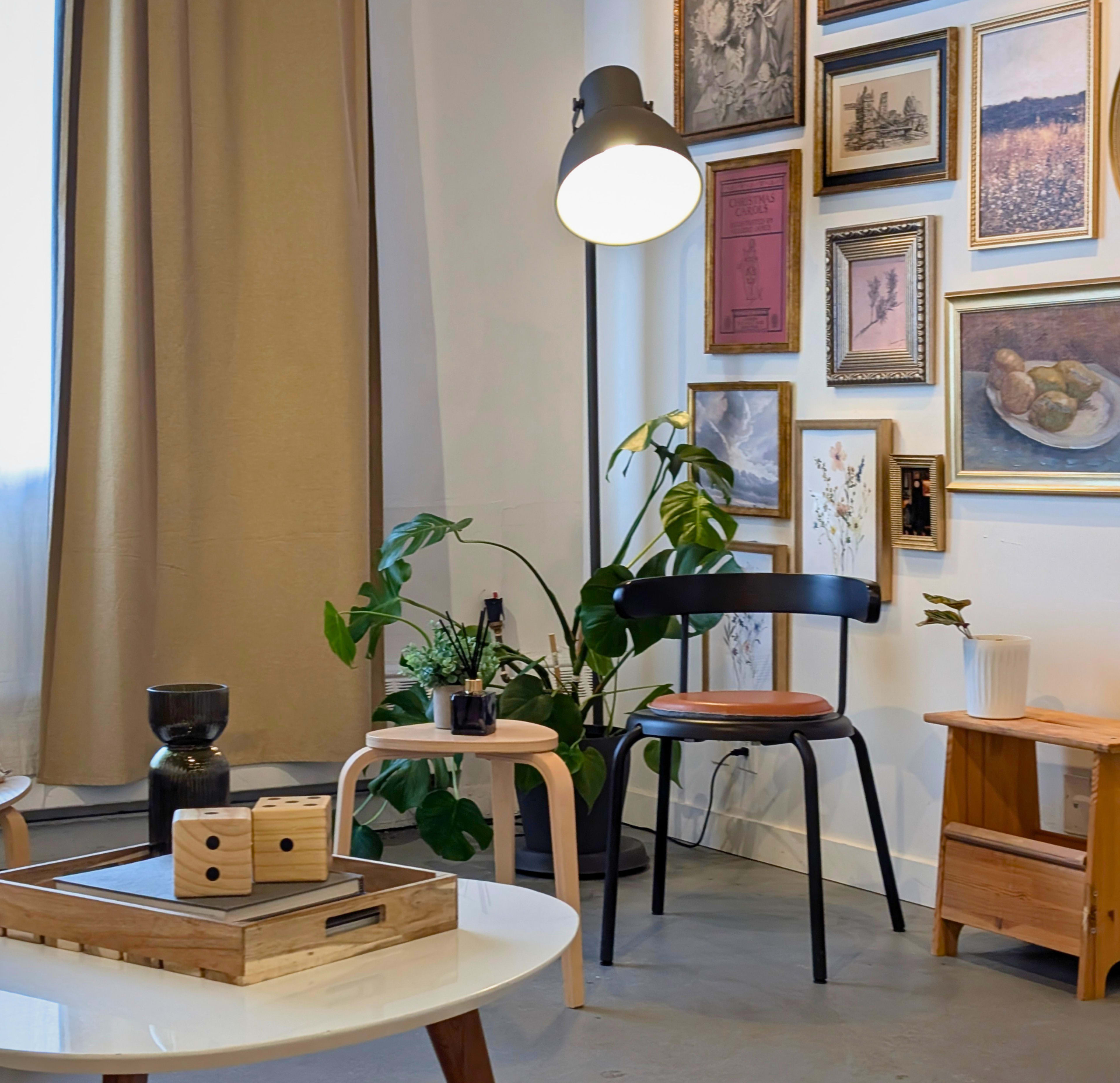 The image shows a stylish interior space featuring a chair, a side table with decorative items, and a wall adorned with various framed pictures.