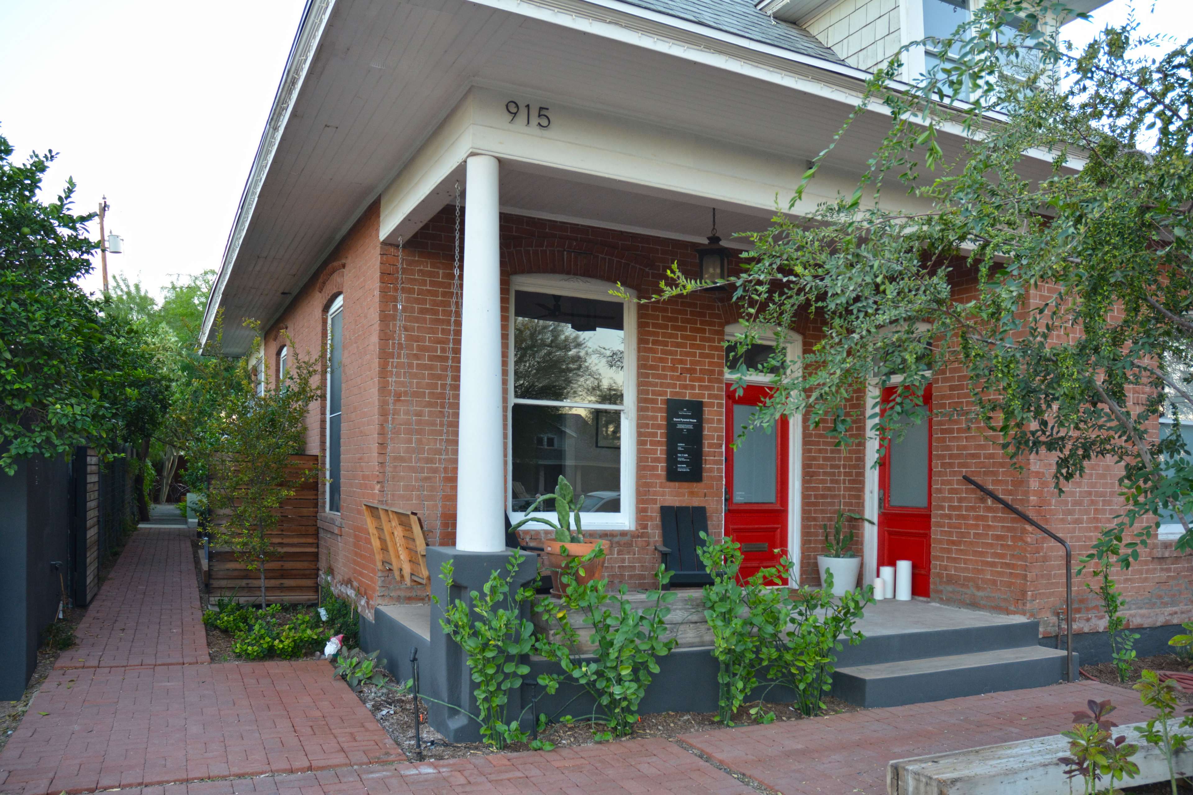 A brick house with red doors and a landscaped front walkway leading to the entrance.
