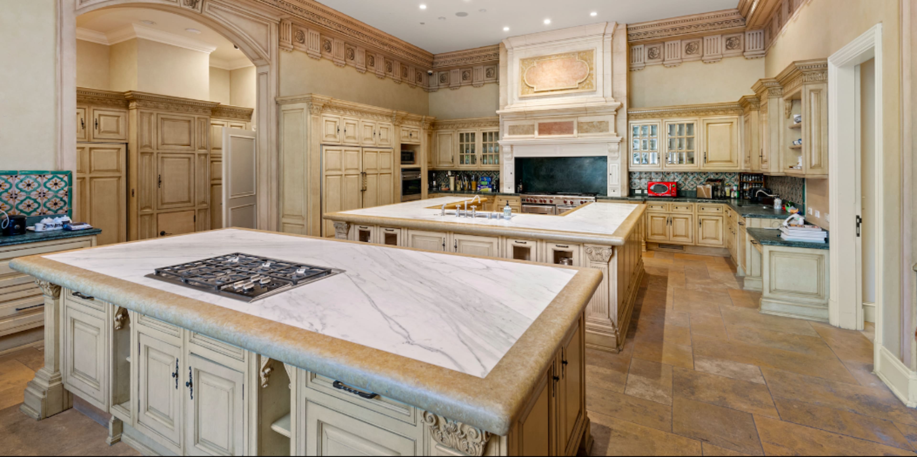 The image shows a spacious, elegantly designed kitchen with multiple islands and light-colored cabinetry.