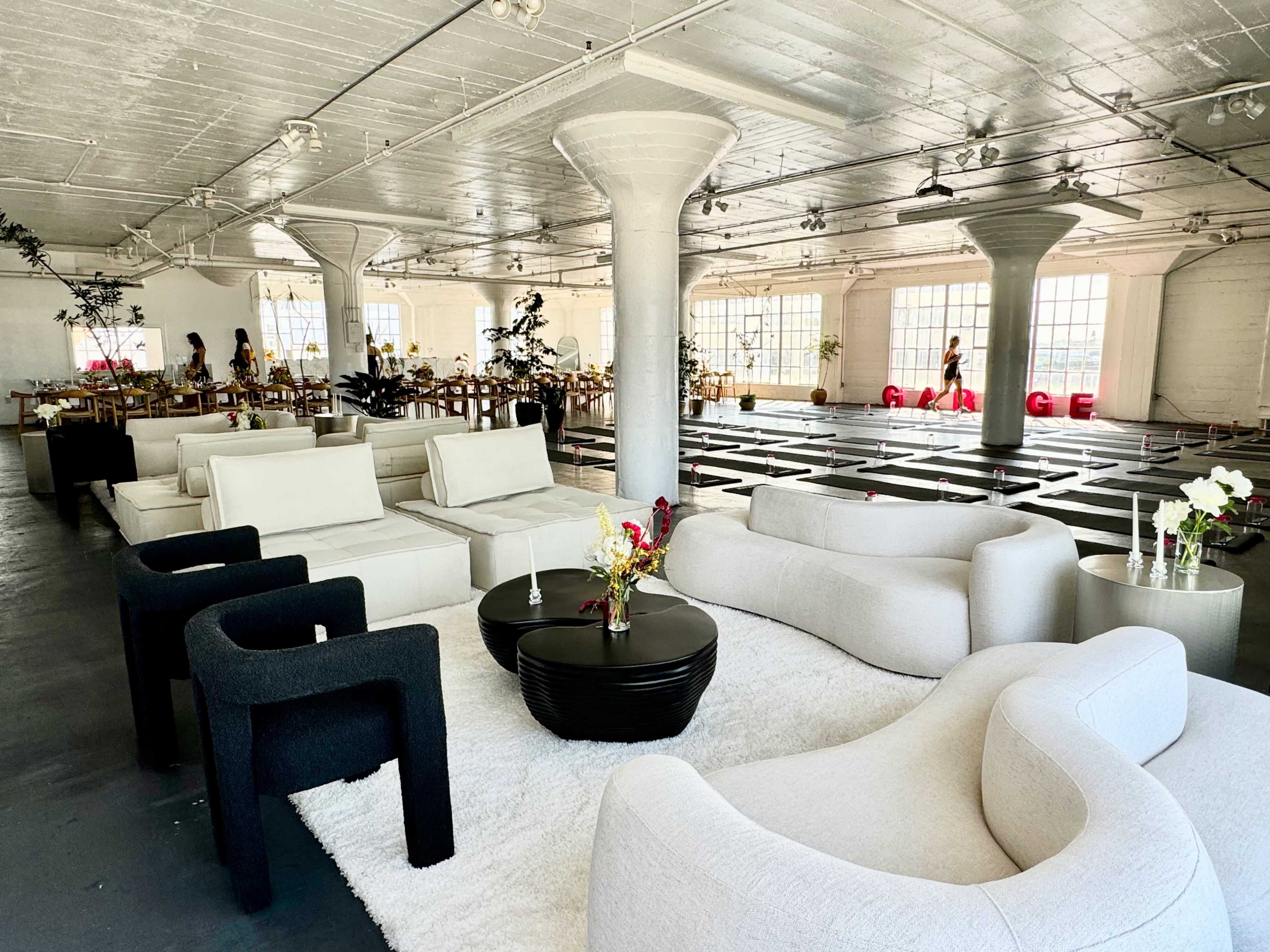 A spacious modern interior with white furniture, large windows, and a dining area set with tables and chairs.