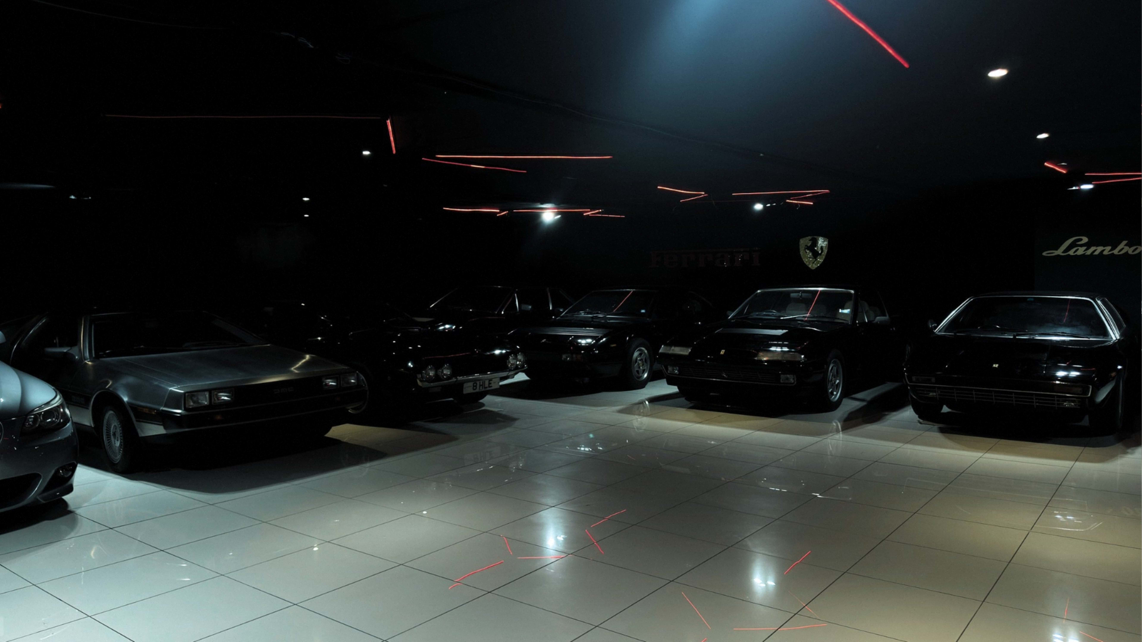 A collection of vintage and luxury cars is displayed under dim lighting in a dark showroom.