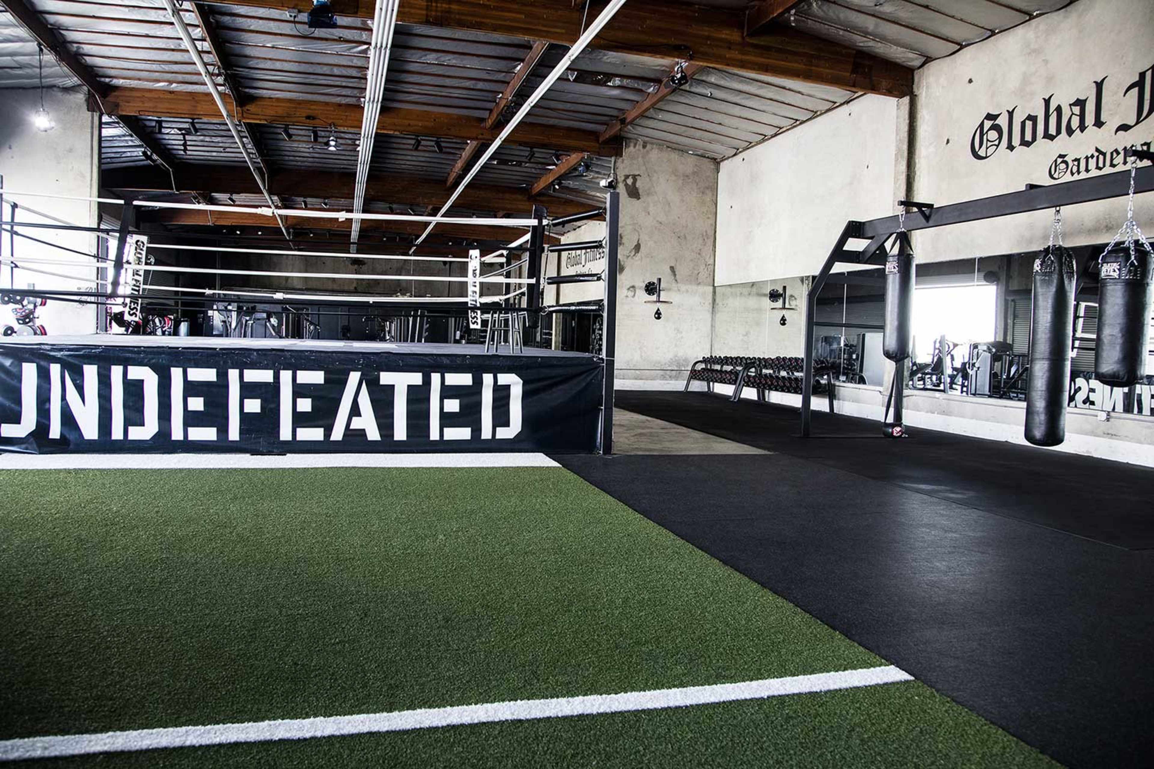 A boxing gym with a ring, bags for training, and a green turf area, all within a spacious industrial-style interior.