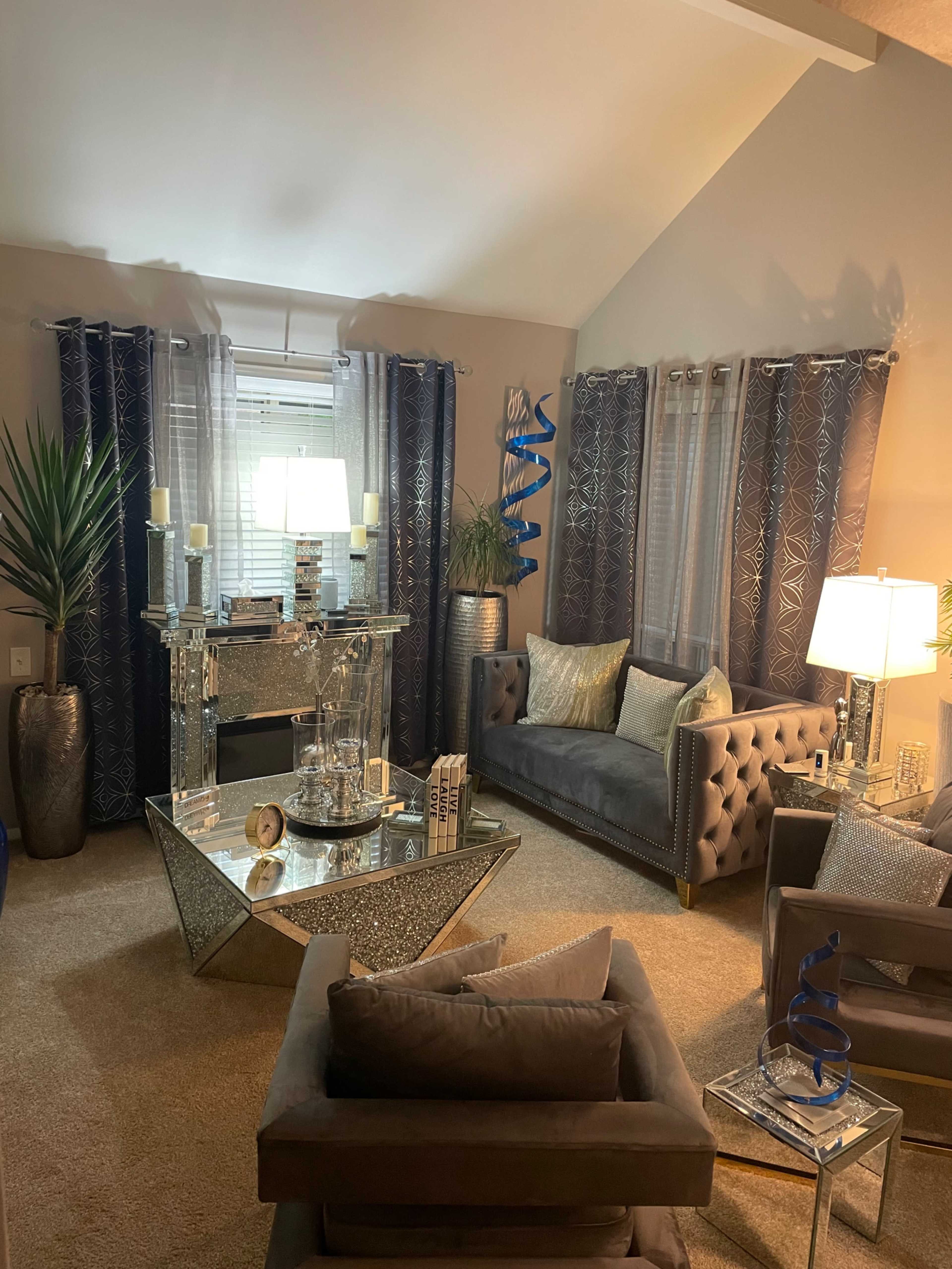 A contemporary living room features a gray sofa, a glass coffee table, and decorative elements including plants and lamps.