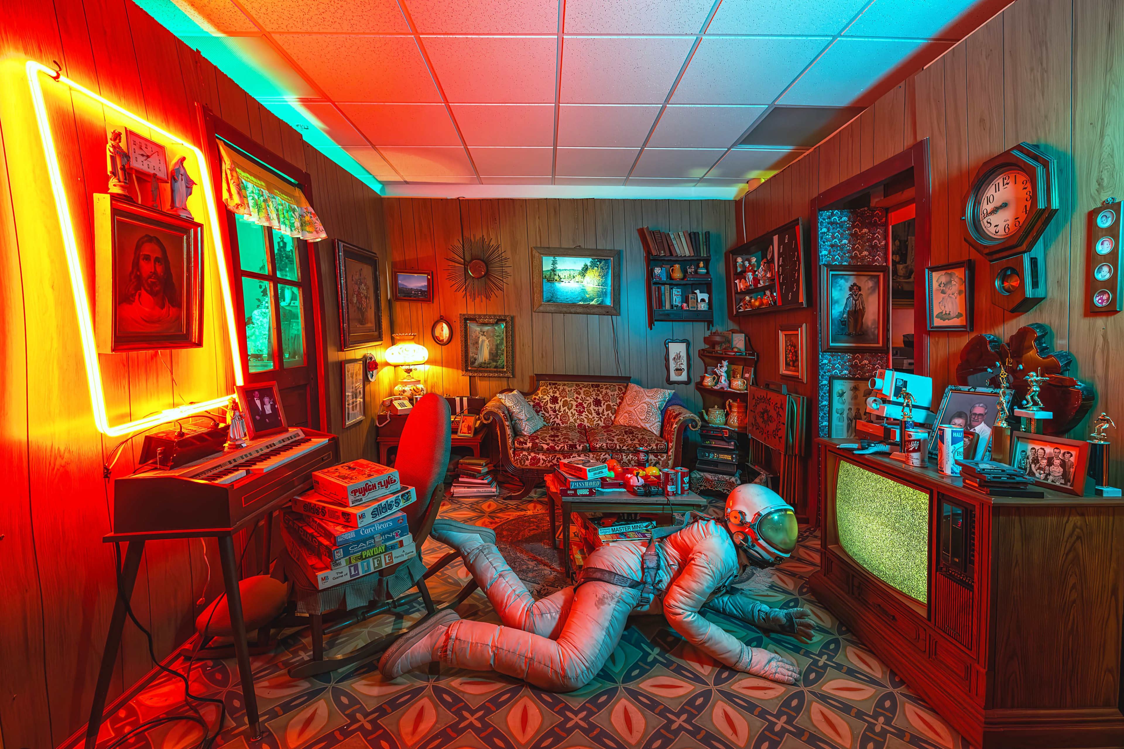 A retro-themed room features a figure in a silver spacesuit crawling across the floor in front of an old television set, surrounded by vintage furniture and decorations.