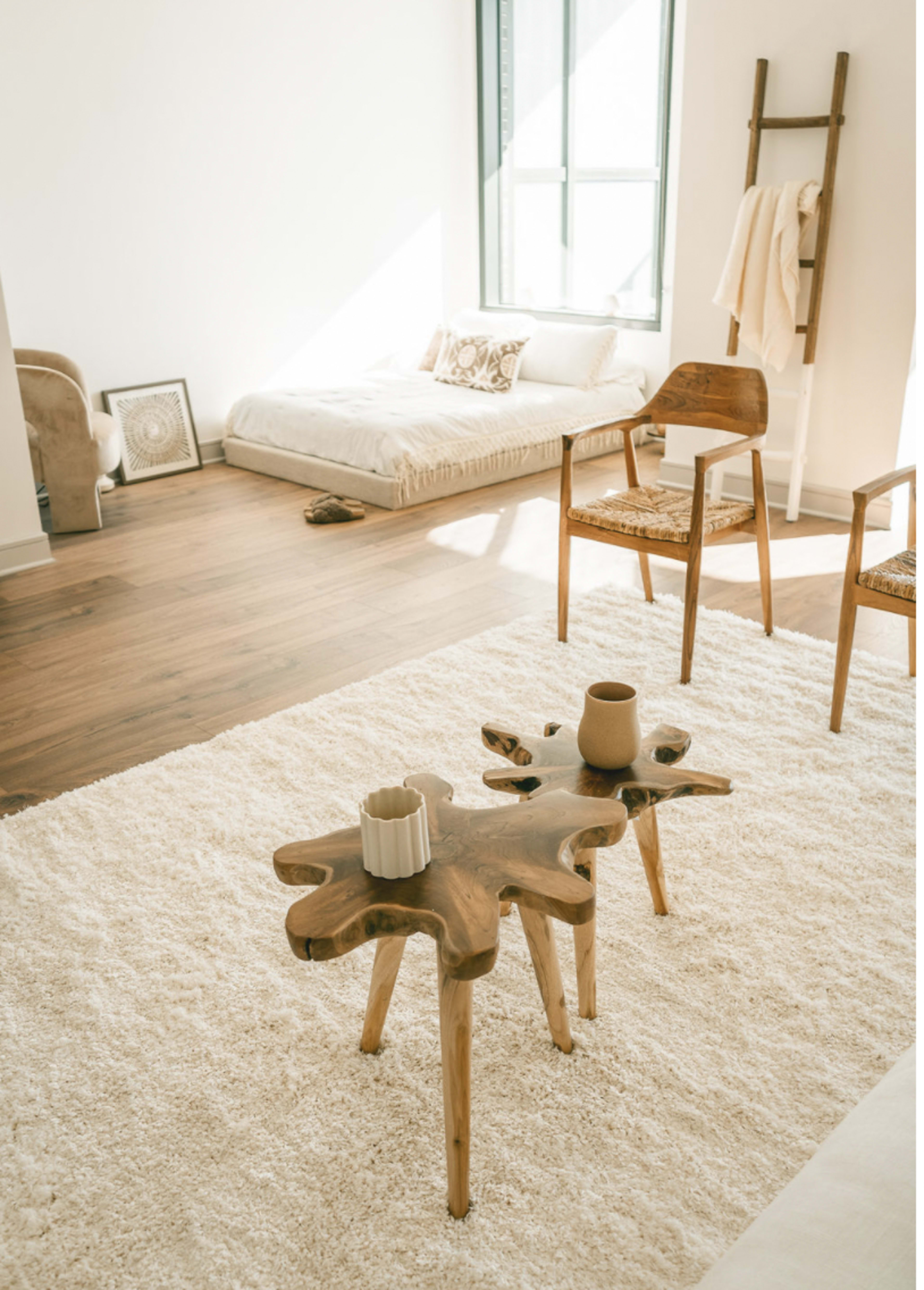 A minimalist living space with a wooden coffee table, two chairs, and a futon in the background, all set on a light-colored rug.