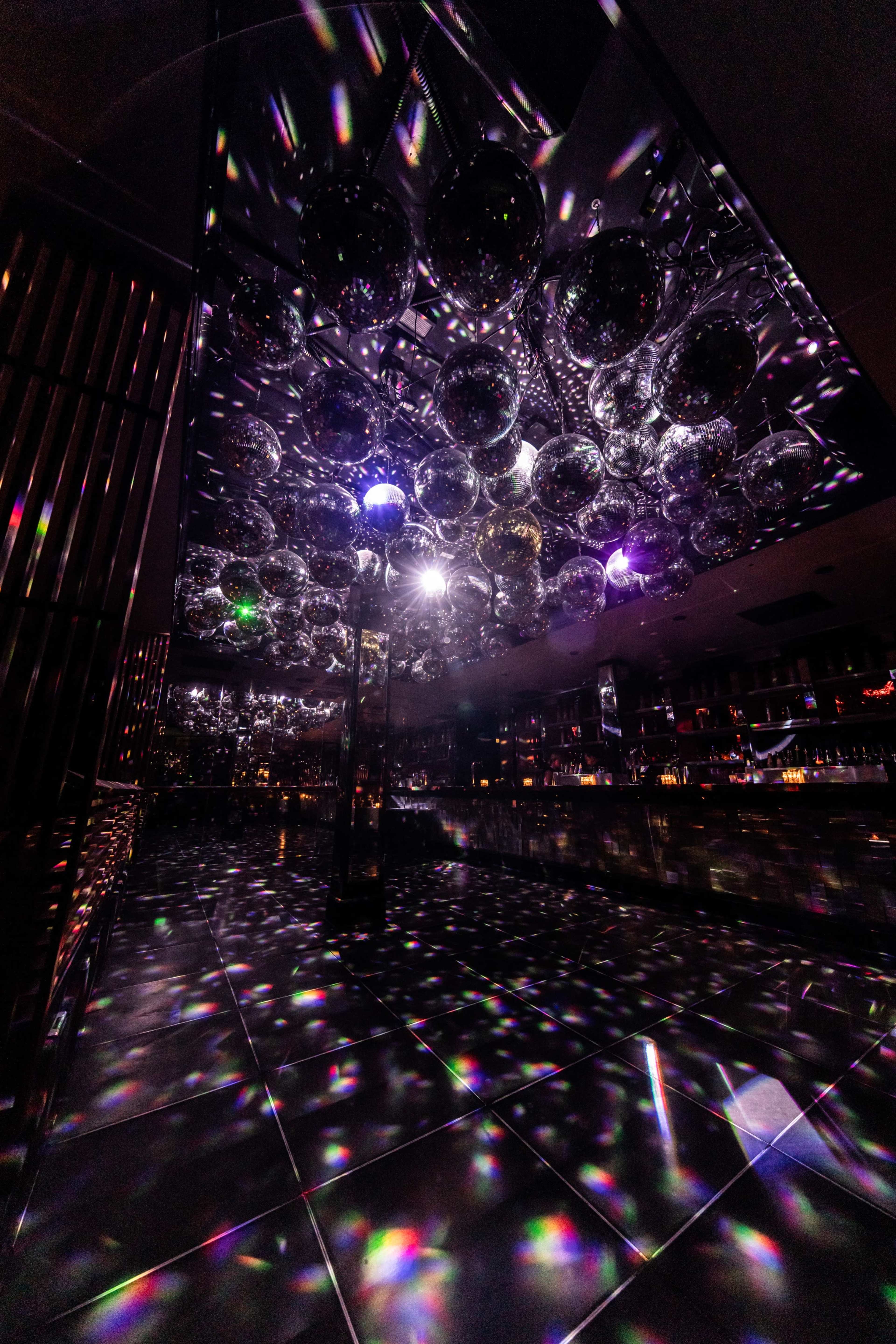 A dimly lit space with a ceiling covered in reflective disco balls, casting colorful light patterns on the floor.