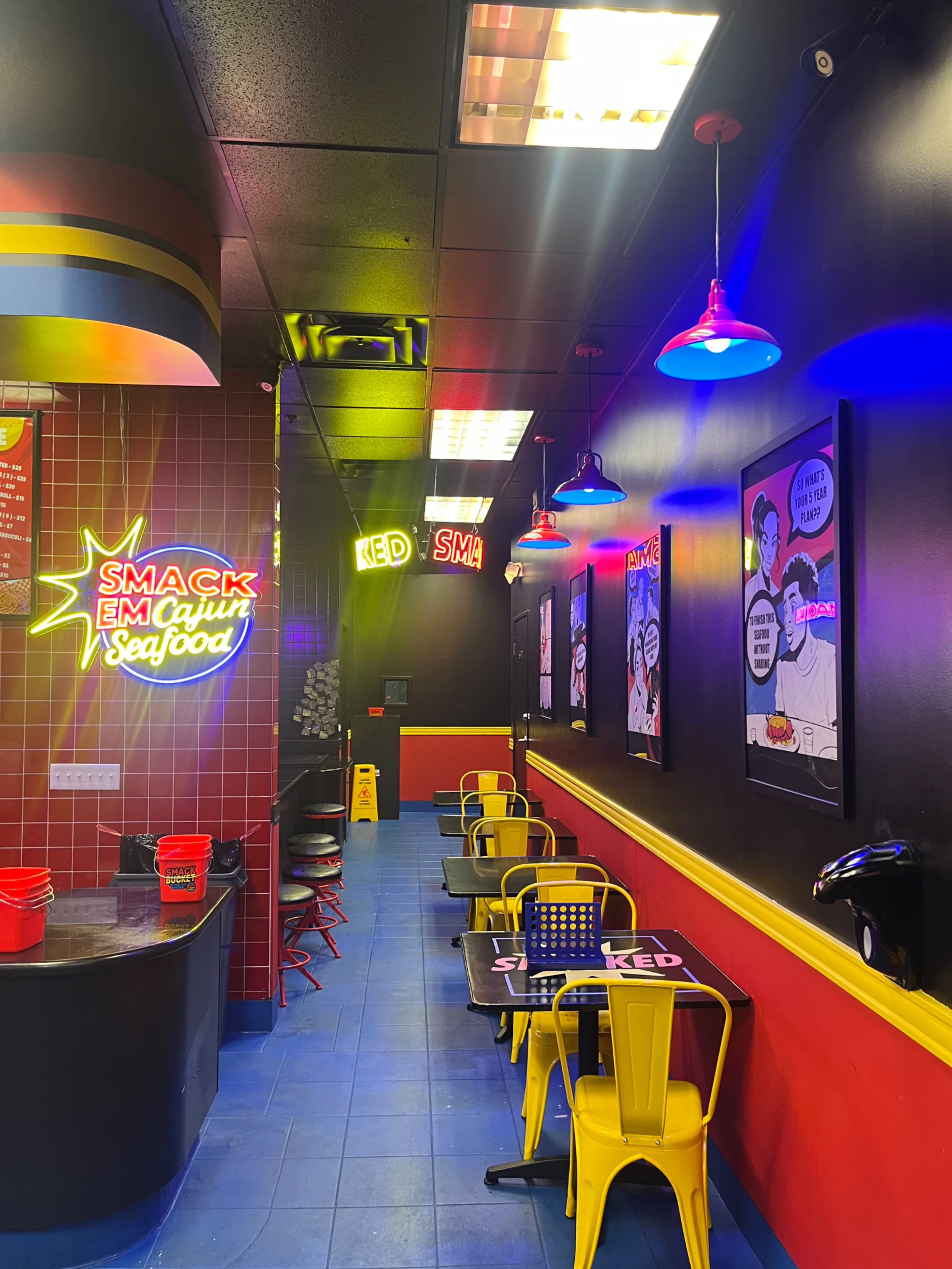 The image shows a brightly colored seafood restaurant interior featuring neon signs, black walls, and colorful seating arrangements.