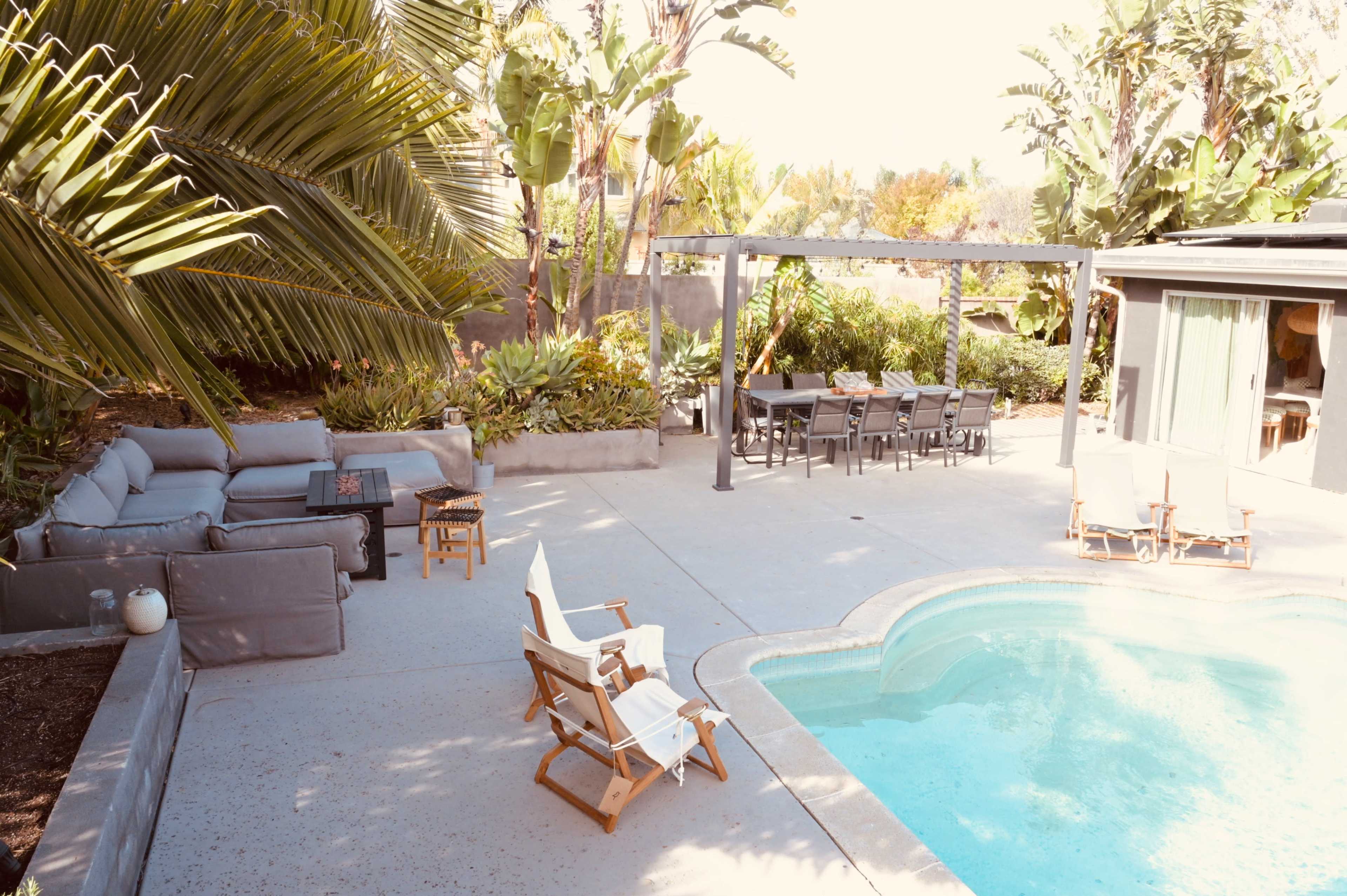The image shows a backyard with a swimming pool, surrounded by lounge chairs, a dining area, and tropical plants.