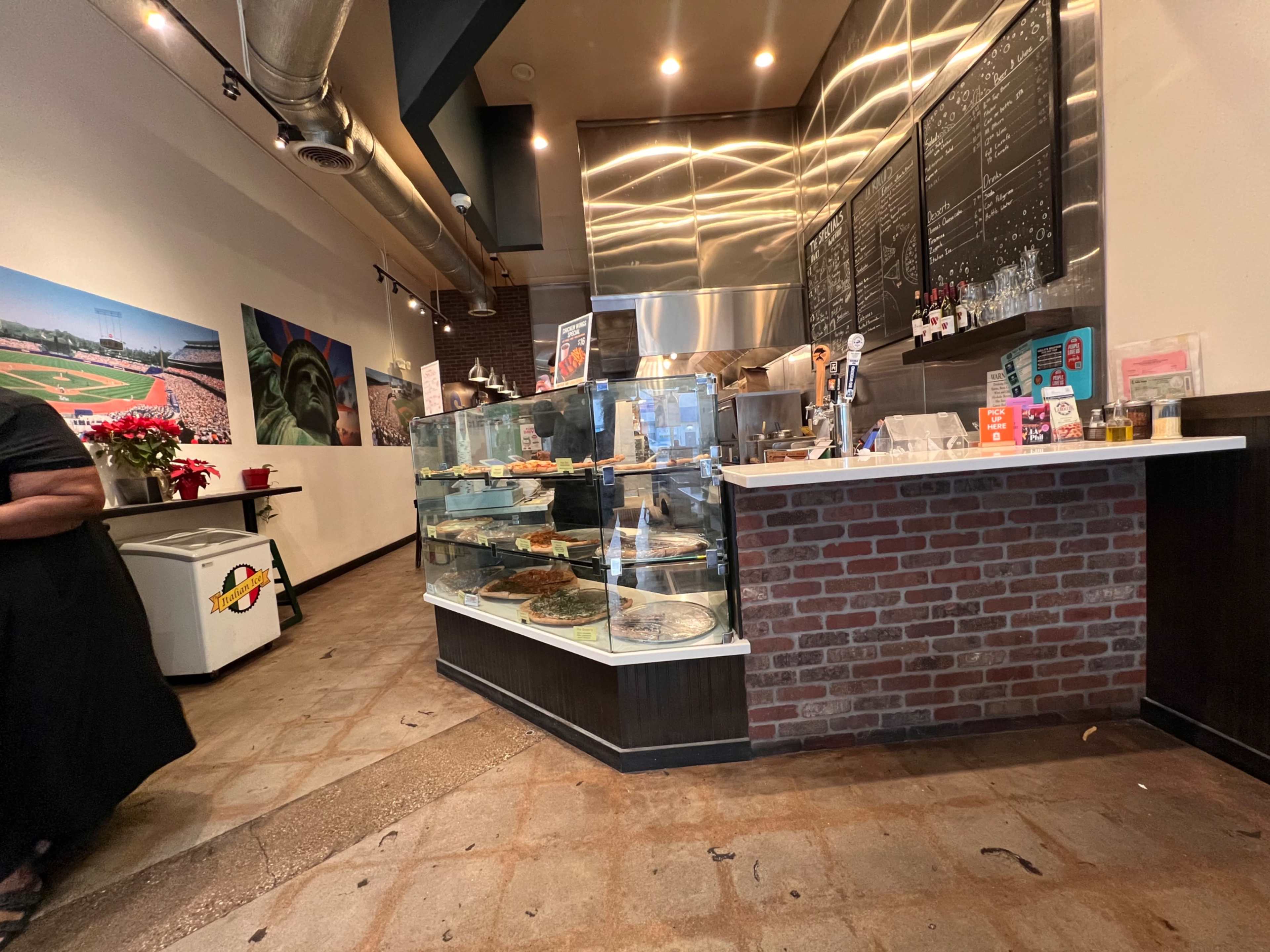 The image shows a café interior featuring a display case of food items, a service counter, and exposed brick walls.