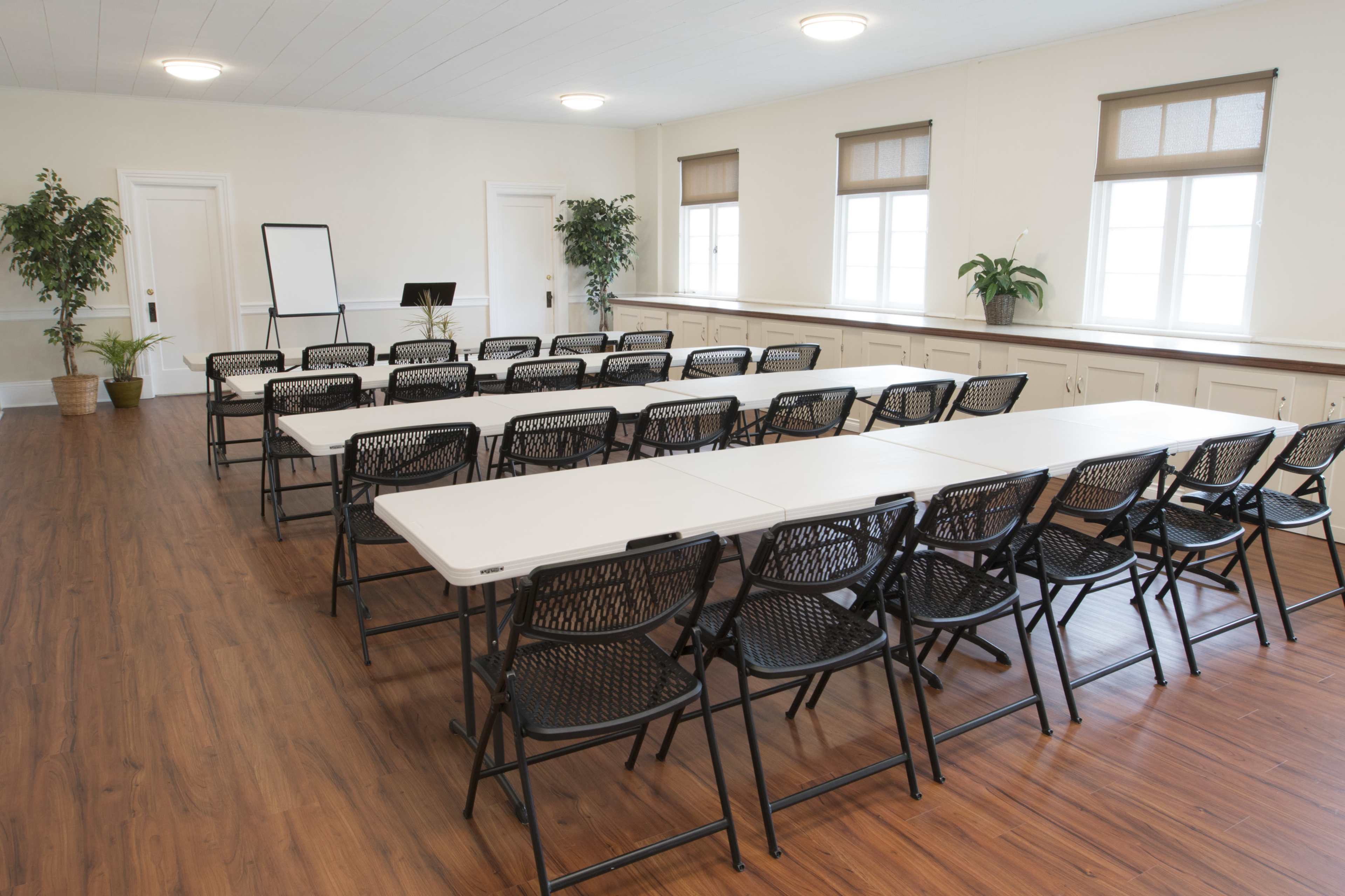 A conference room set up with neatly arranged folding tables and chairs, along with a flip chart and plants.