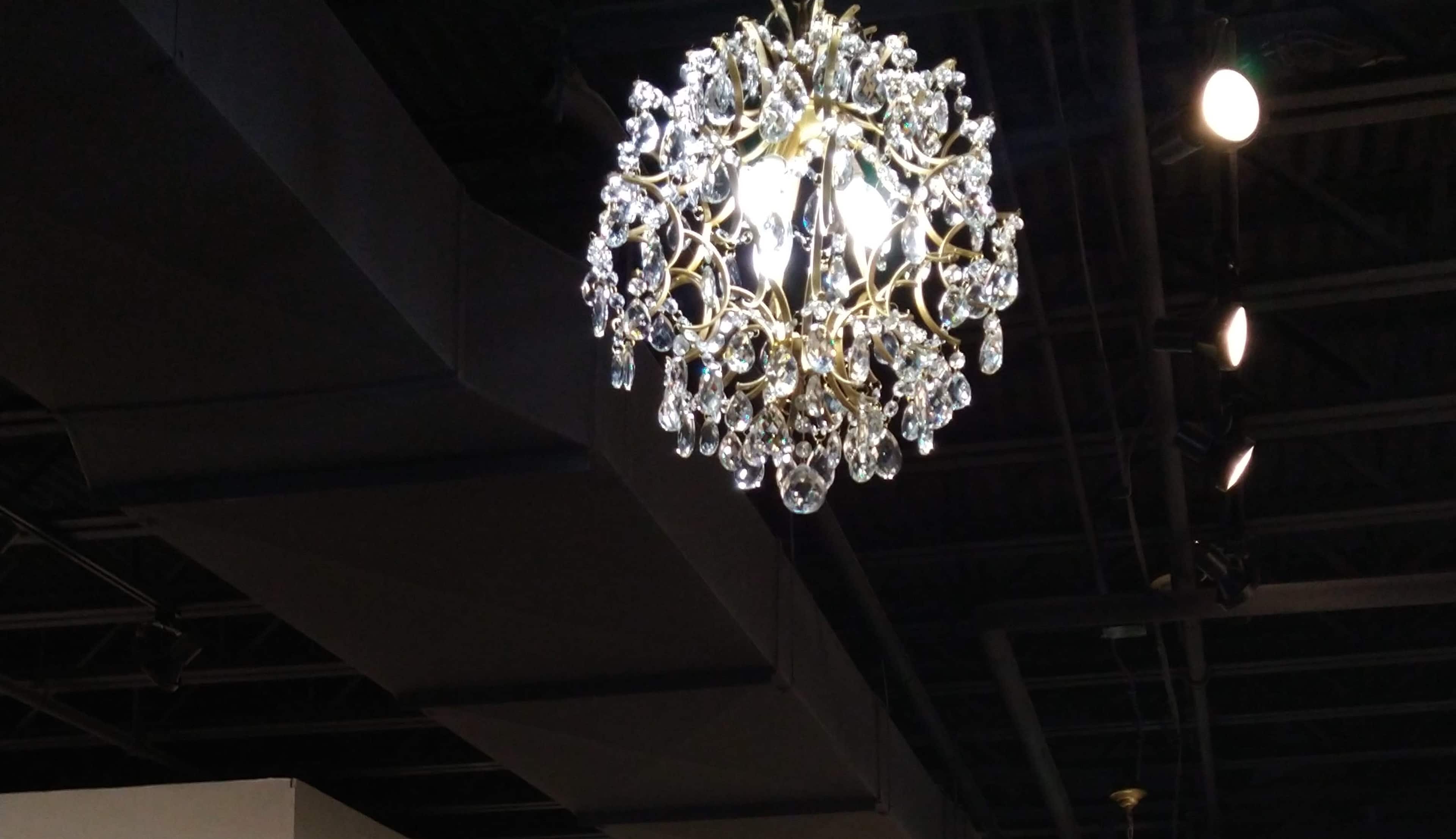 A decorative chandelier with crystal elements hangs from the ceiling in a dimly lit space.