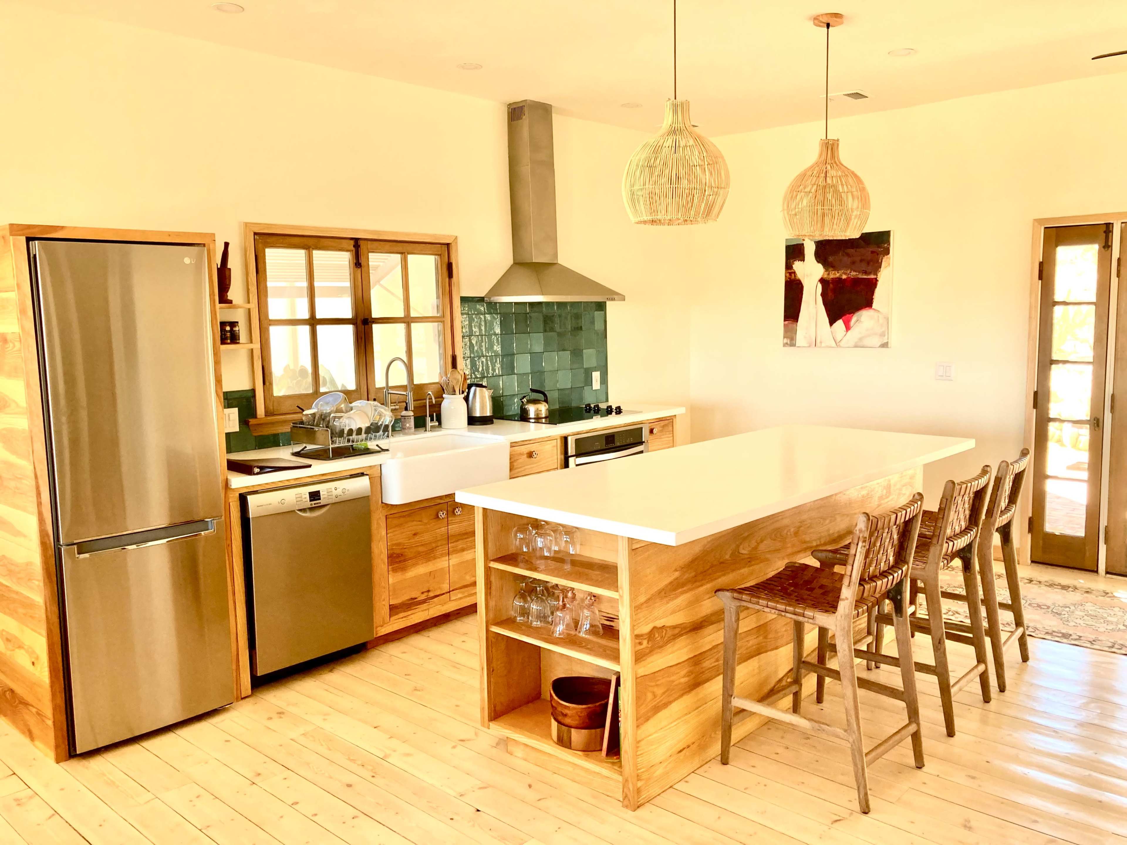 A modern kitchen features a large island with bar stools, stainless steel appliances, wooden cabinetry, and pendant lighting.