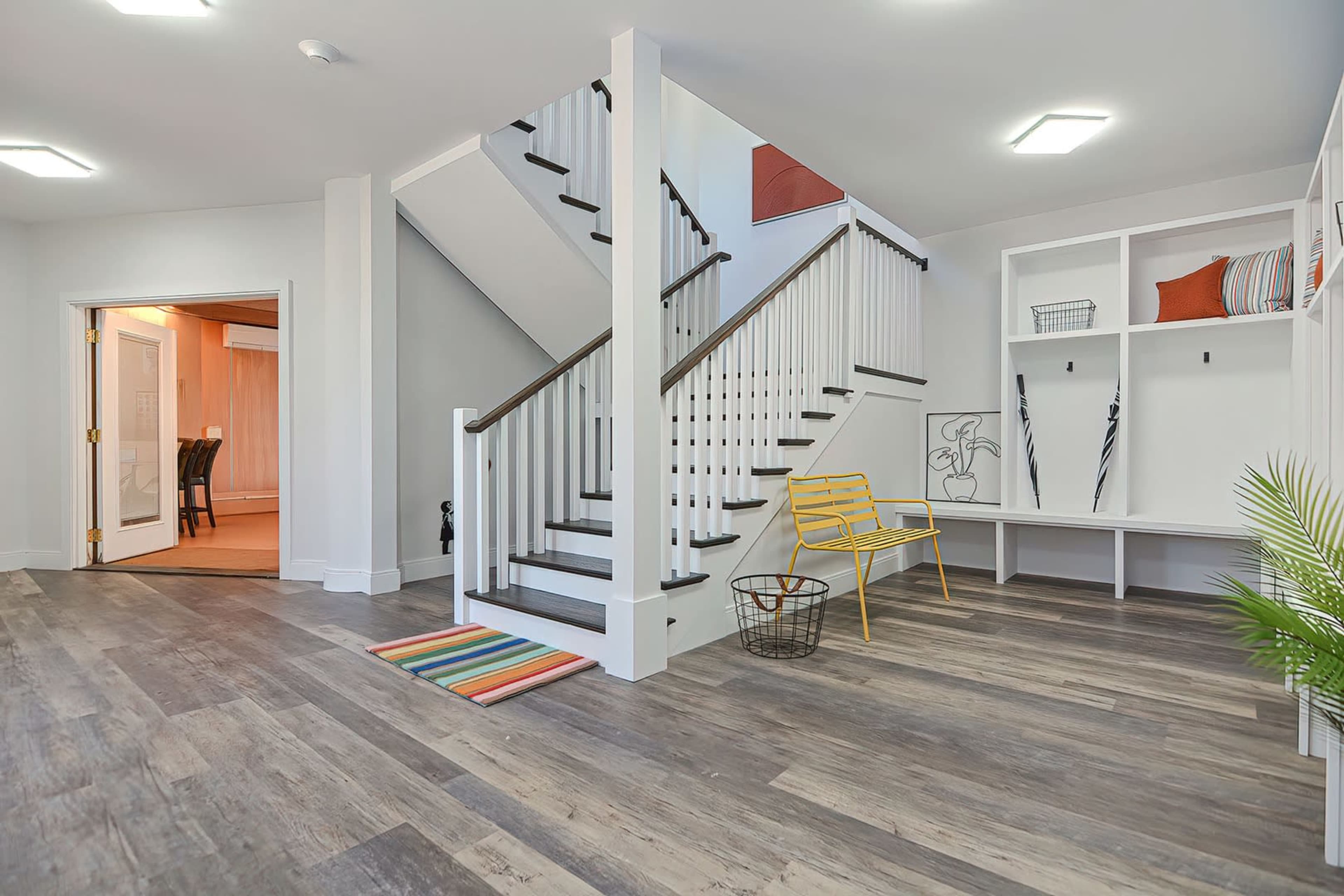 The image shows a well-lit foyer featuring a staircase, a yellow chair, and a bench with cubbies against the wall.