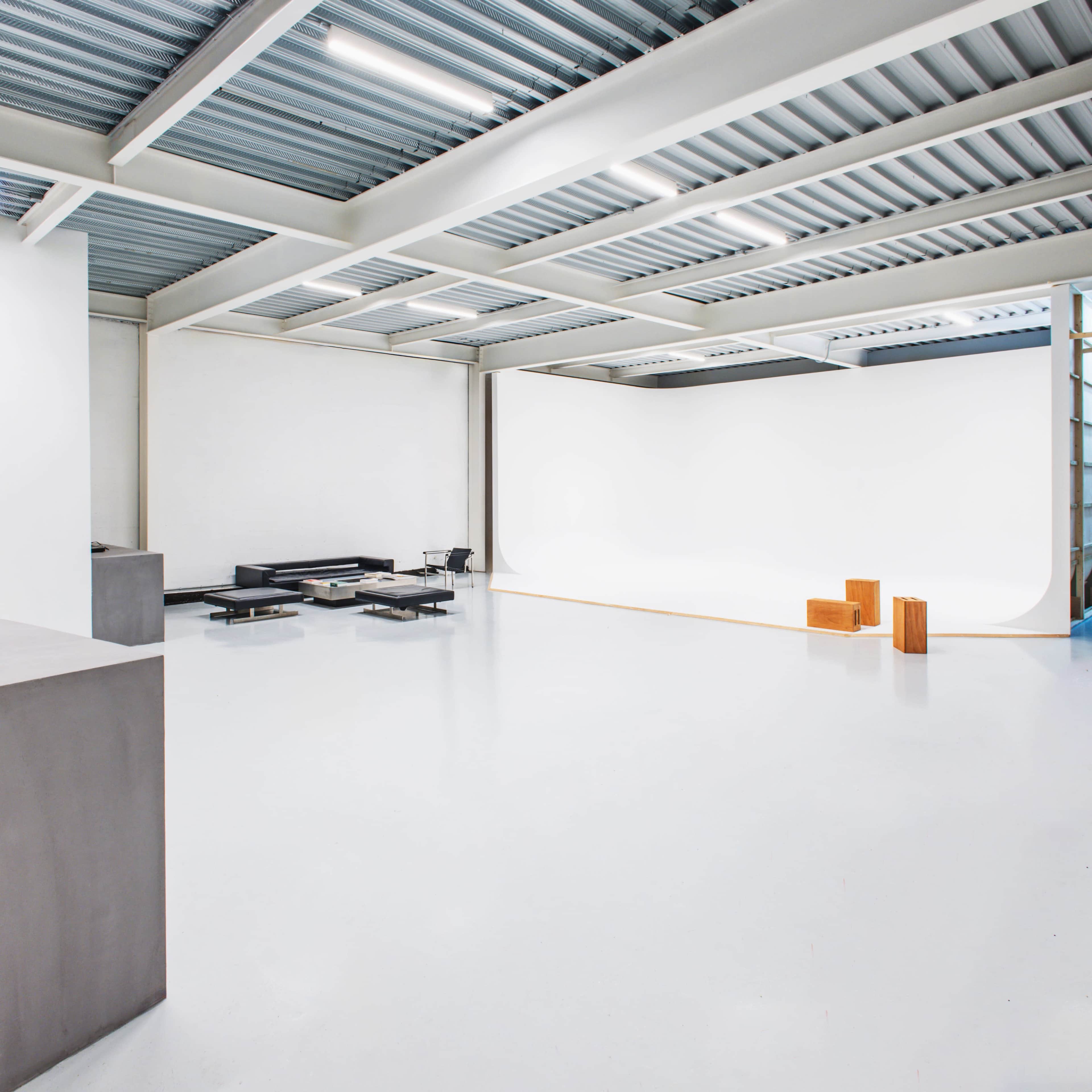 A spacious, well-lit studio features a white backdrop, minimalist furniture, and a polished concrete floor.