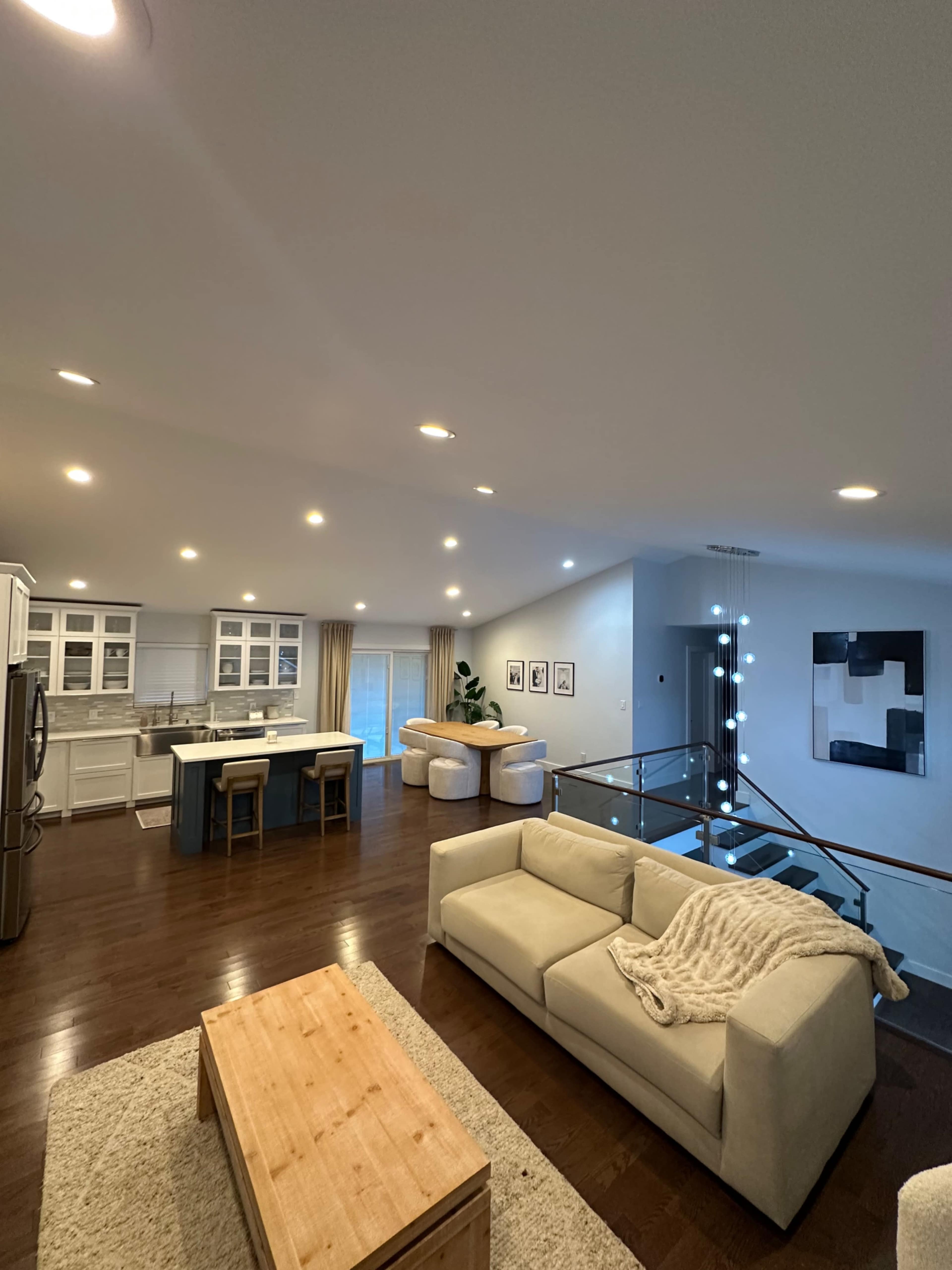 The image shows a modern, open-concept living space featuring a kitchen, dining area, and a cozy seating arrangement with large windows allowing natural light.