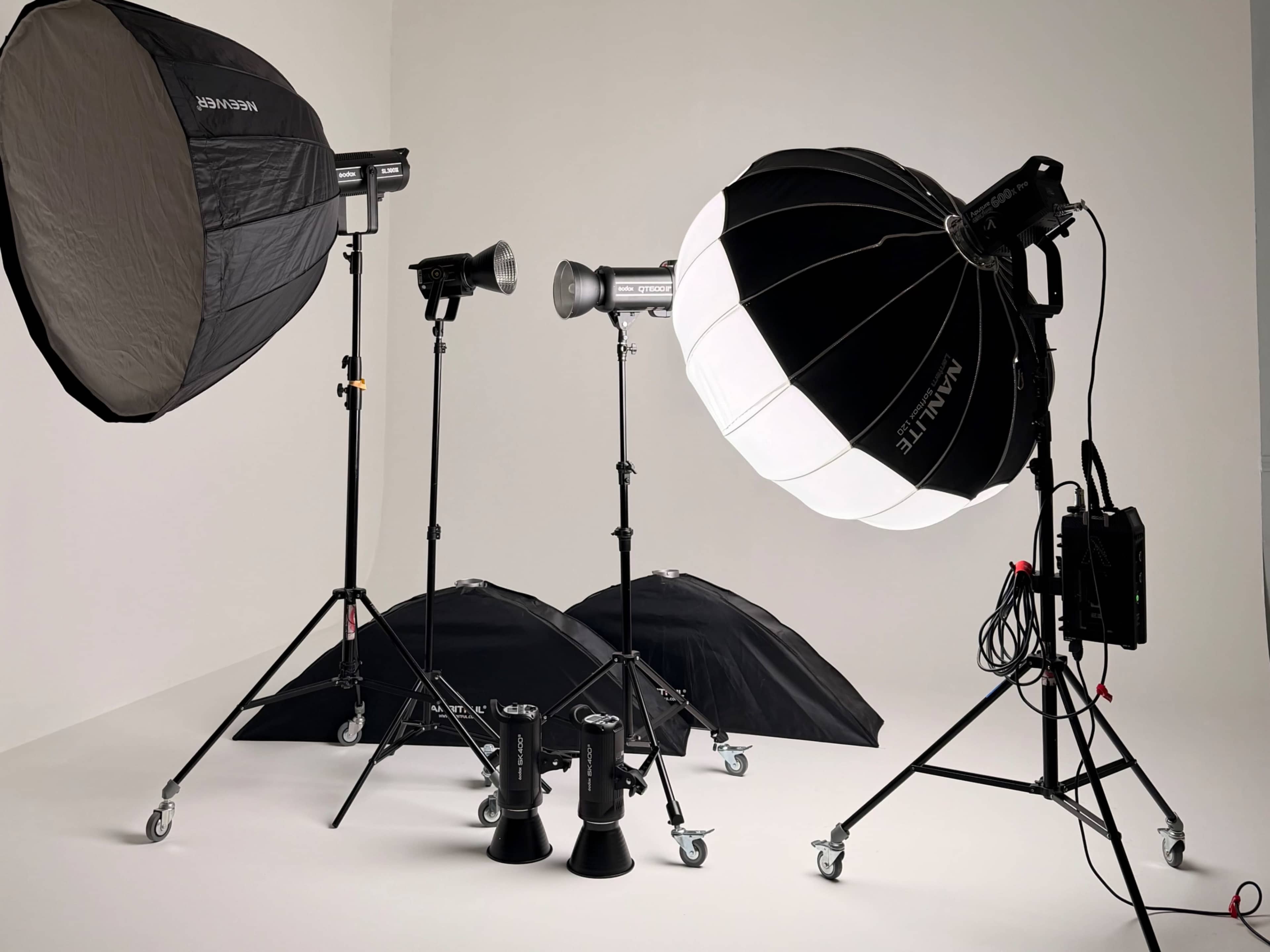 The image features various photography lighting equipment, including softboxes, flash units, and light stands arranged in a plain studio setting.