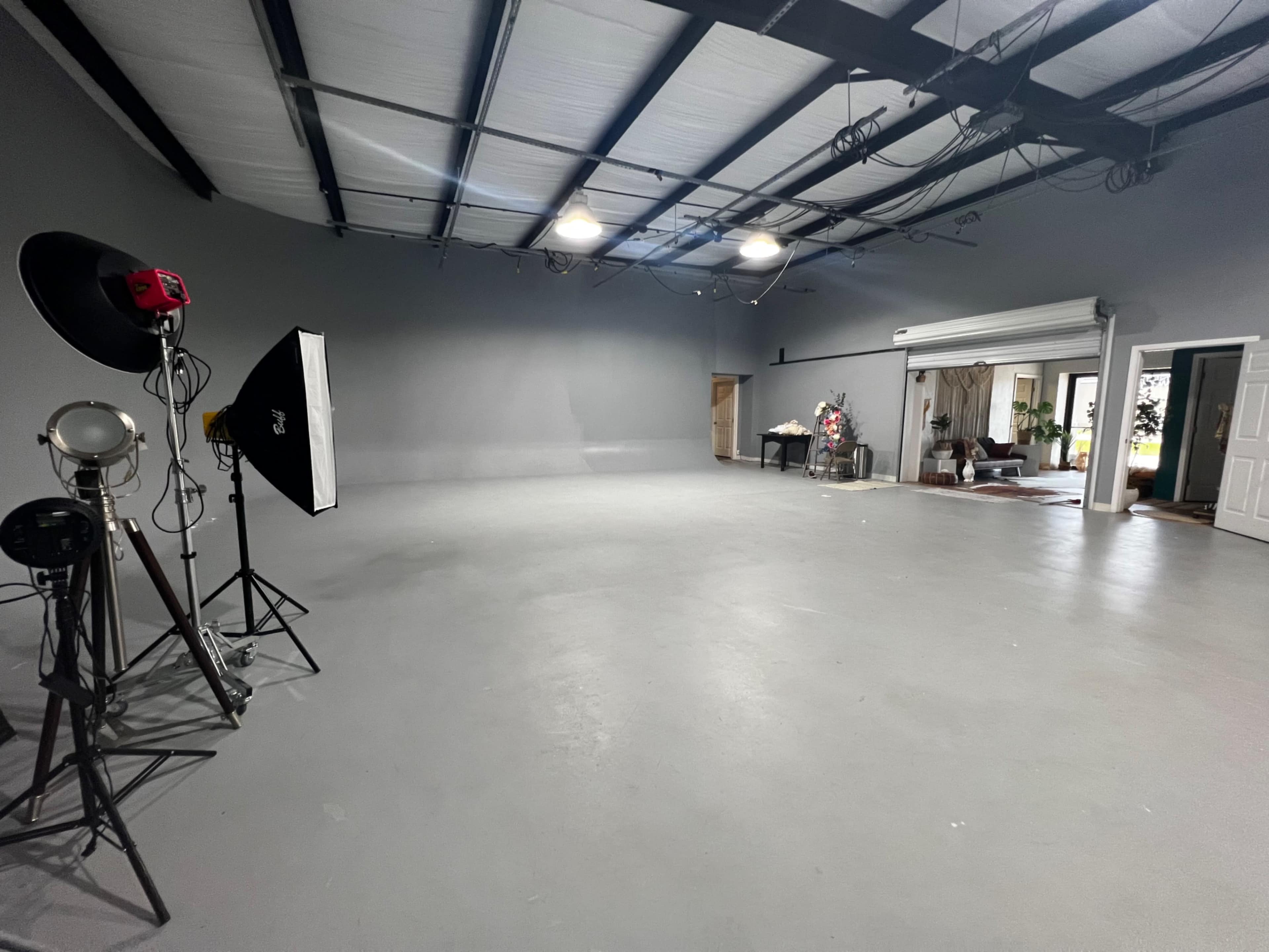 A large, empty studio space with gray walls, overhead lighting, and various photography equipment on the left side.
