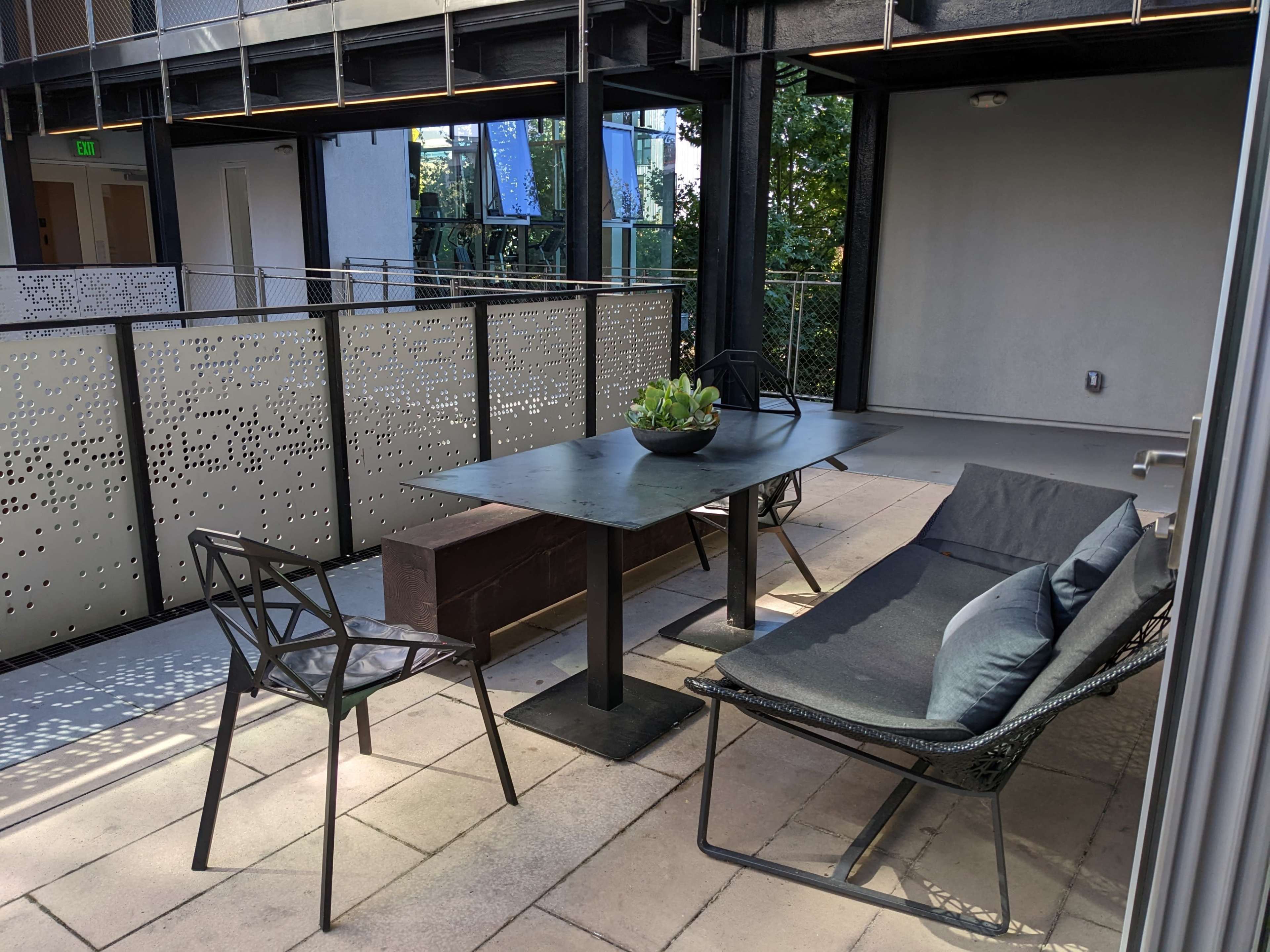 A modern outdoor patio area with a table, chairs, and a planter, surrounded by decorative metal fencing.