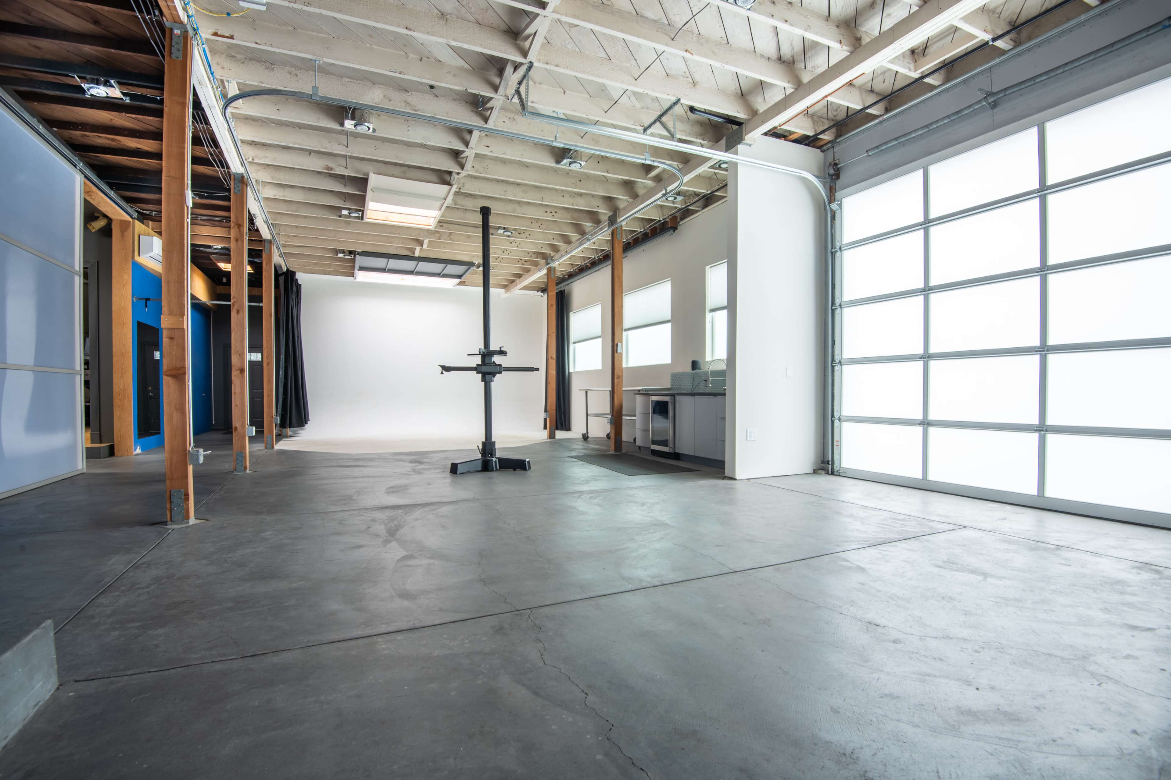 An empty studio space with concrete flooring, wooden beams, and a garage-style door.